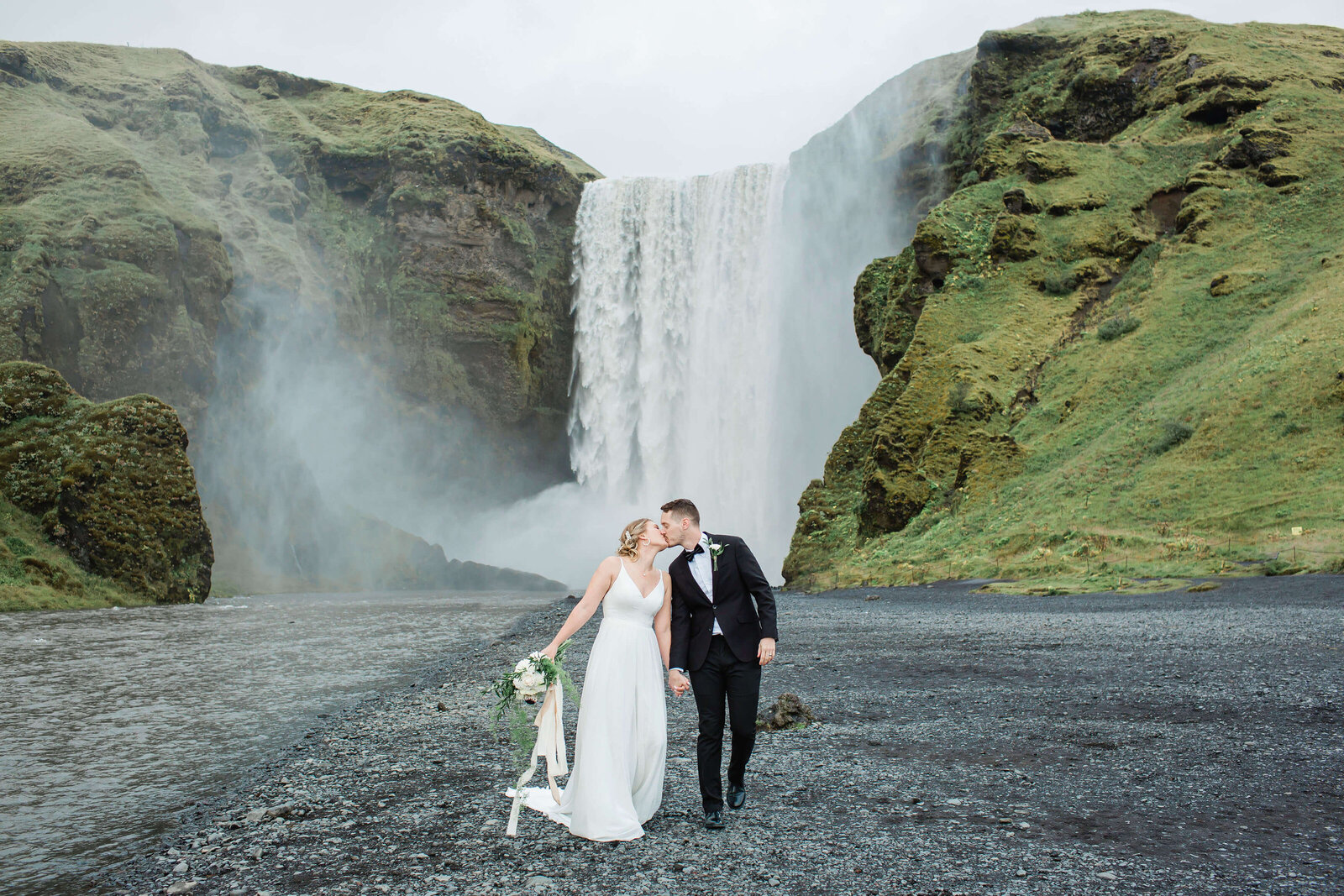 Michael and Nicole holding hands in their wedding attire in front of Skogafoss waterfall in Iceland during their elopement 