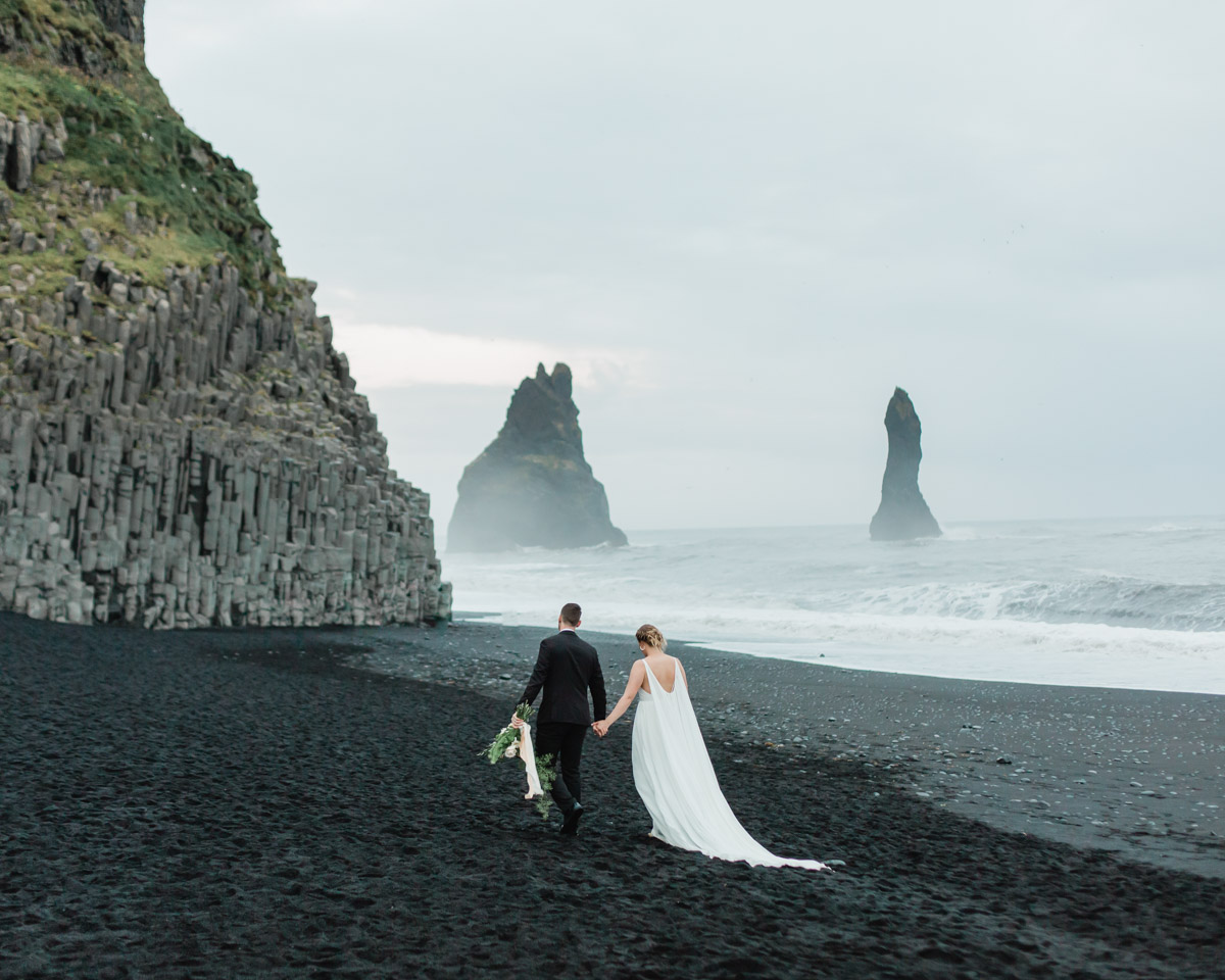 Michael and Nicole hand in hand walking on black sand beach in Iceland during their elopement wedding day 