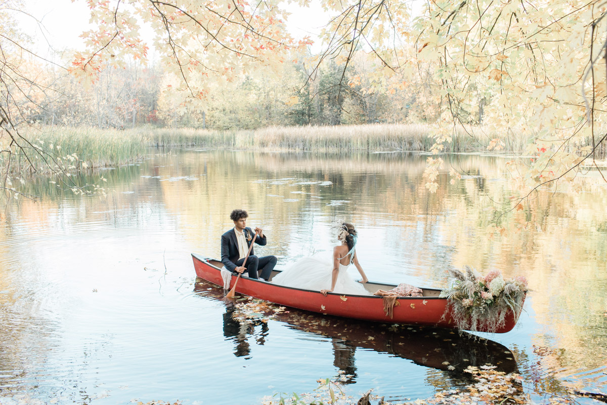 A couple that eloped in Ontario that are canoeing on a private campground pond and enjoying the beauty around them. 