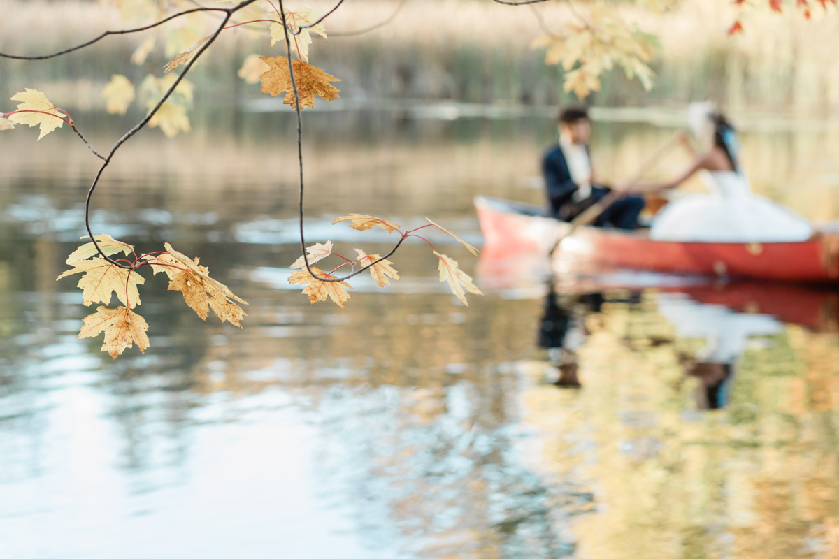 A close up of a leaf branch with a couple paddling behind it during their elopement in Ontario