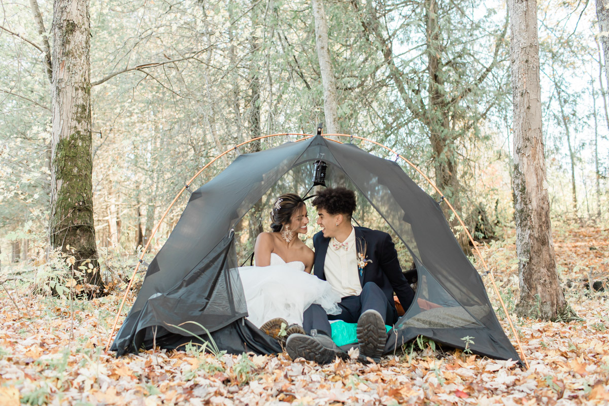 A couple during their camping elopement in Ontario laughing and smiling together in their tent while they're camping