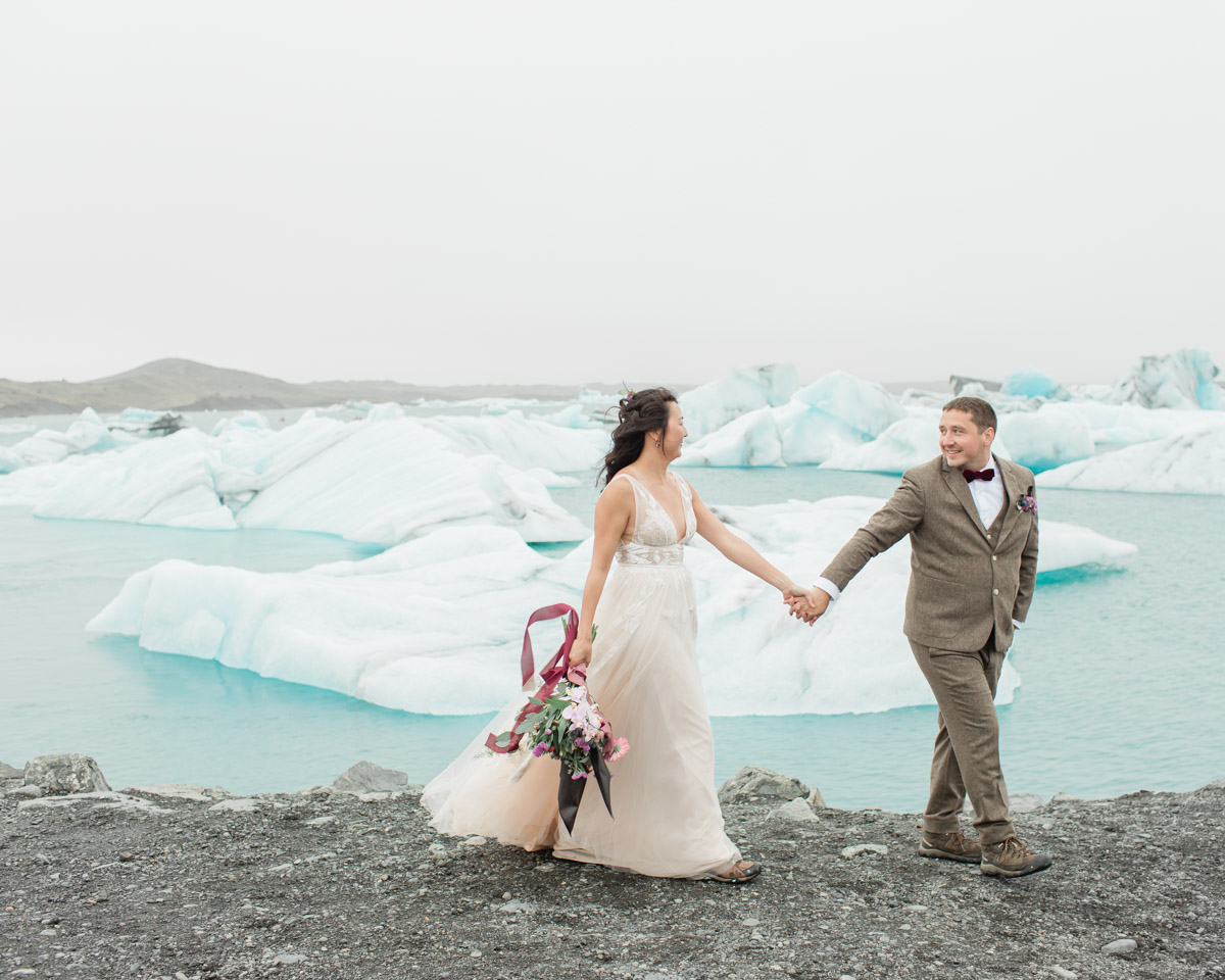 Leah and Darin holding hands and walking in front of glacier lagoon in Iceland