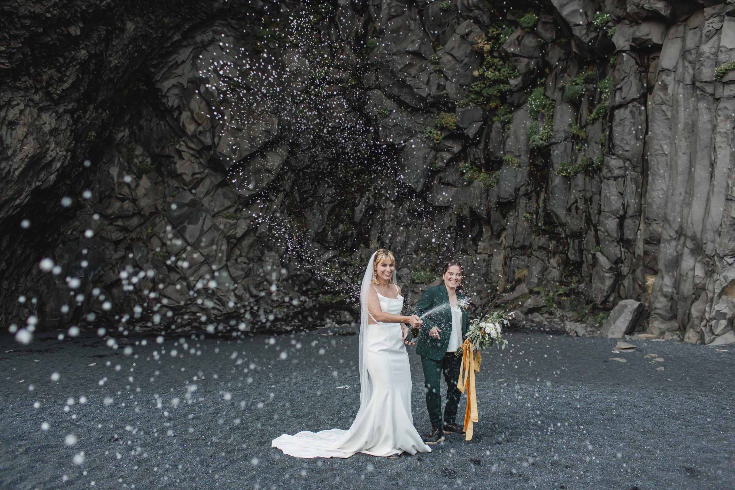 Kili and Joanna celebrating their elopement with champagne on black sand beach in Iceland