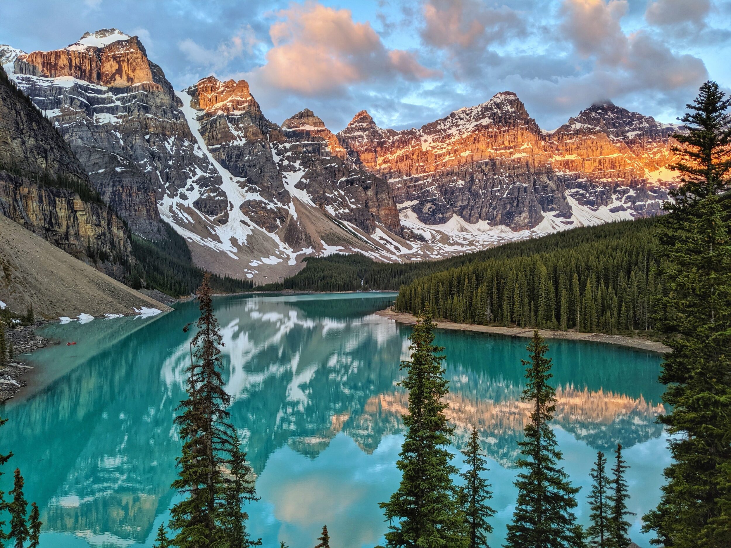 A turquoise lake beneath a Canadian Rocky mountain ridge, nestled amongst a forest of pine trees. 