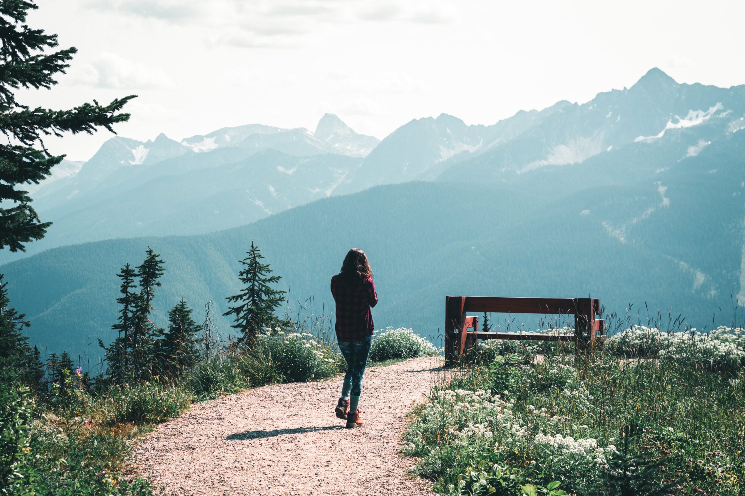 A woman is seen hiking along a dirt path to a bench that overlooks Revelstoke. 