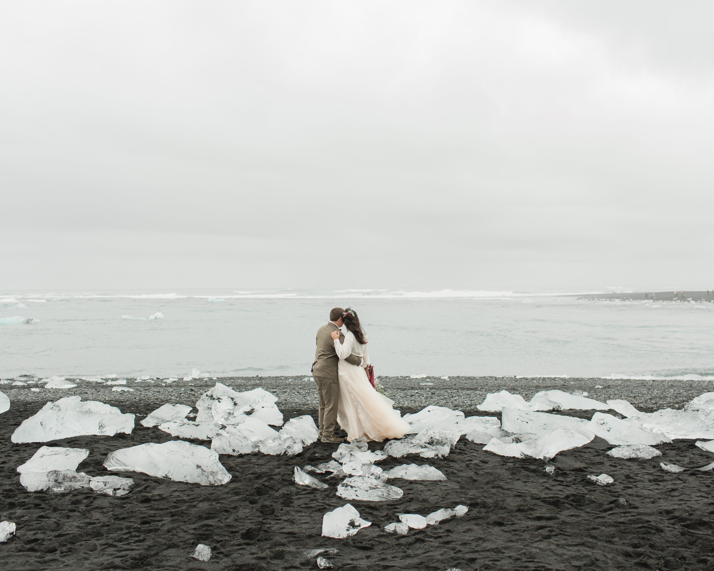 A couple shares a kiss during their wedding ceremony on a beach in Iceland.