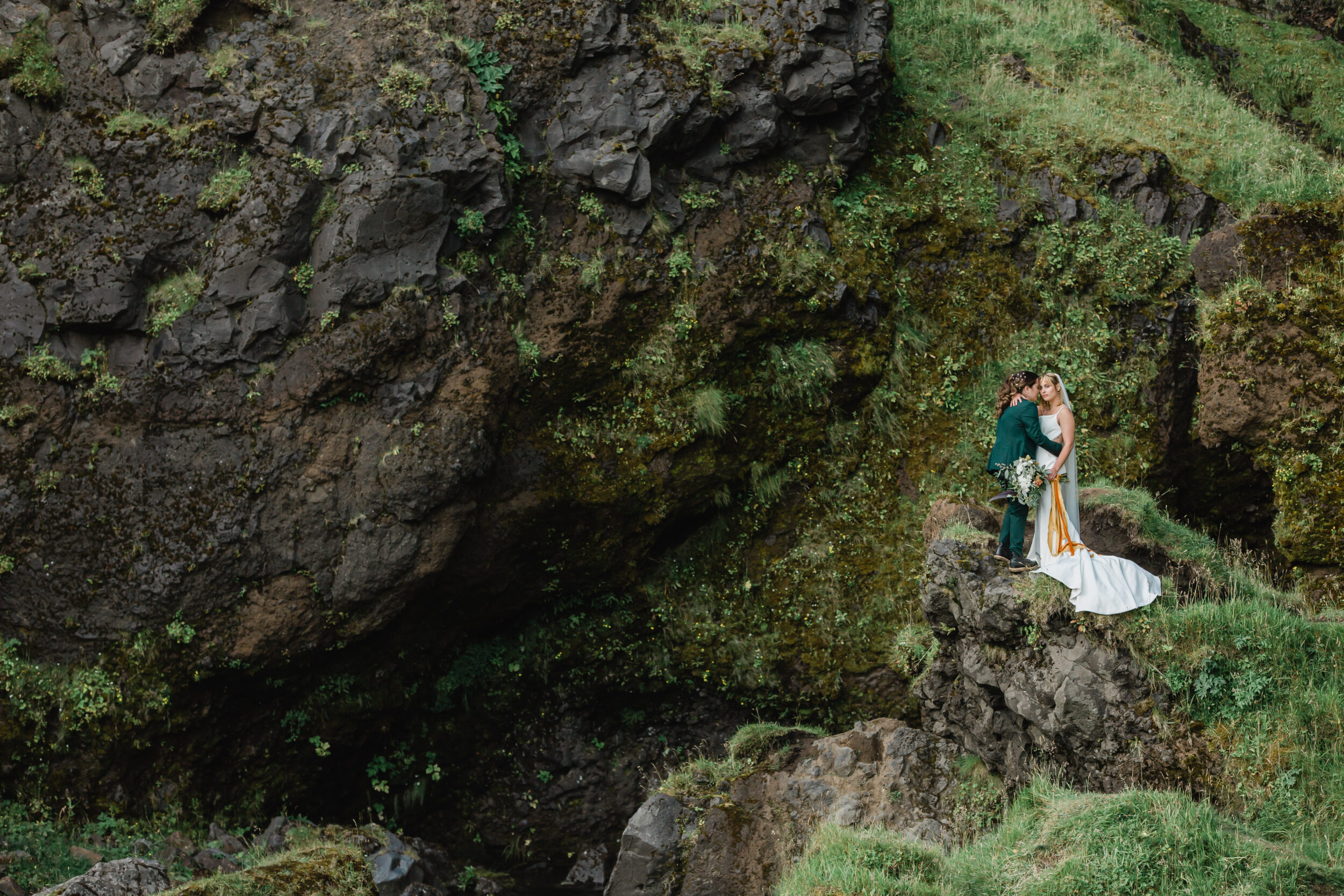 A couple stands beneath a large waterfall during their elopement in Iceland.