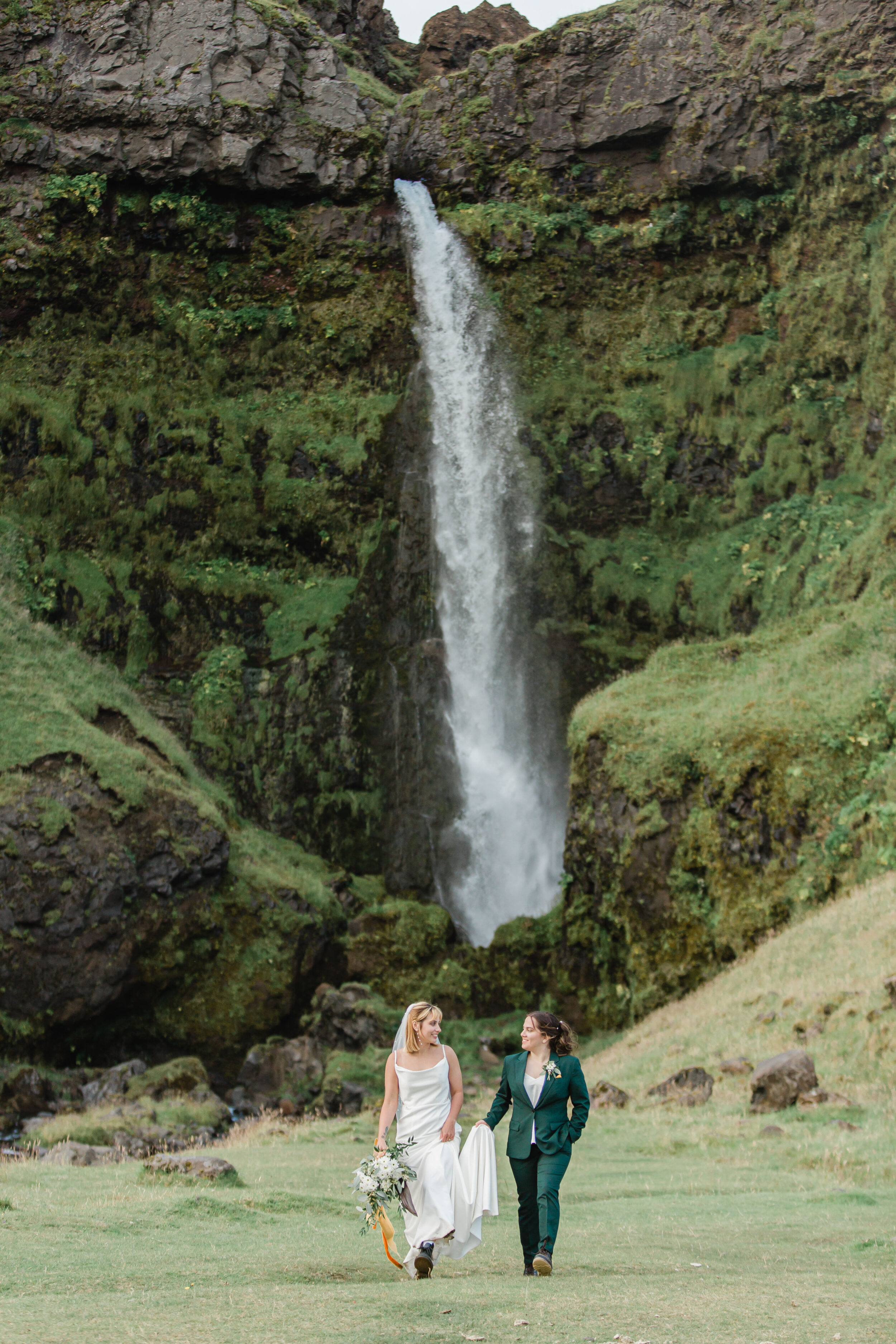 A waterfall is seen in the distance cascading down a cliff with newlyweds in the foreground.