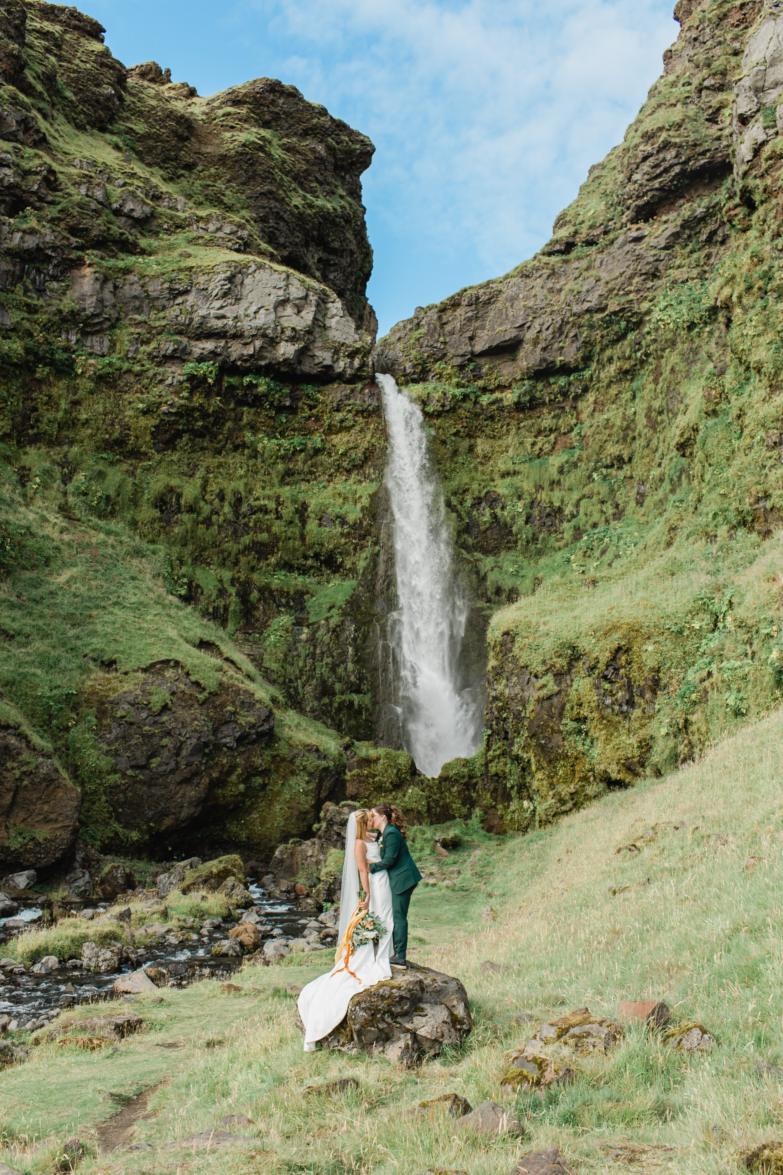 A couple stands beneath a beautiful cascade in Iceland.