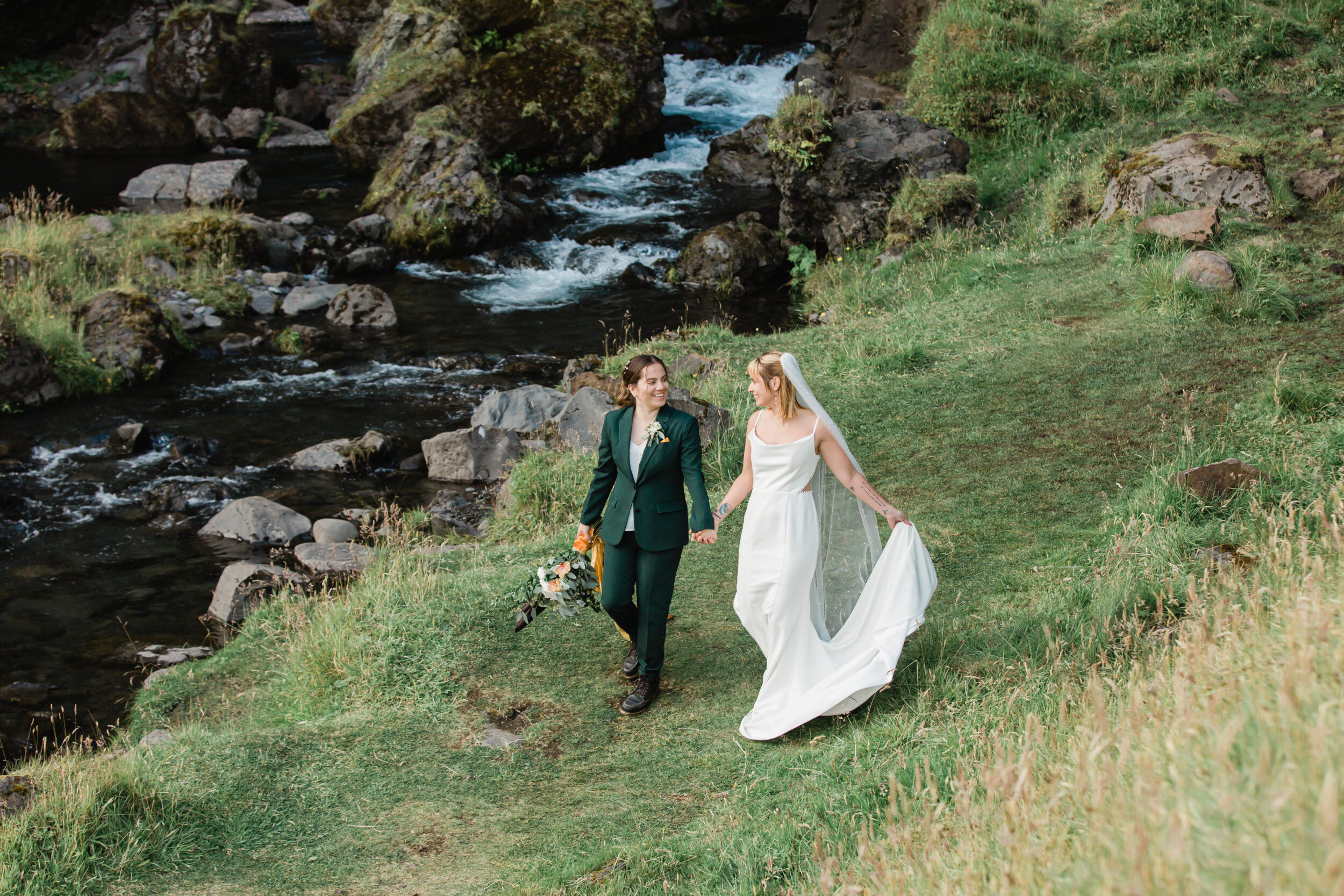 A couple strolls along a stream in wedding attire in Iceland.