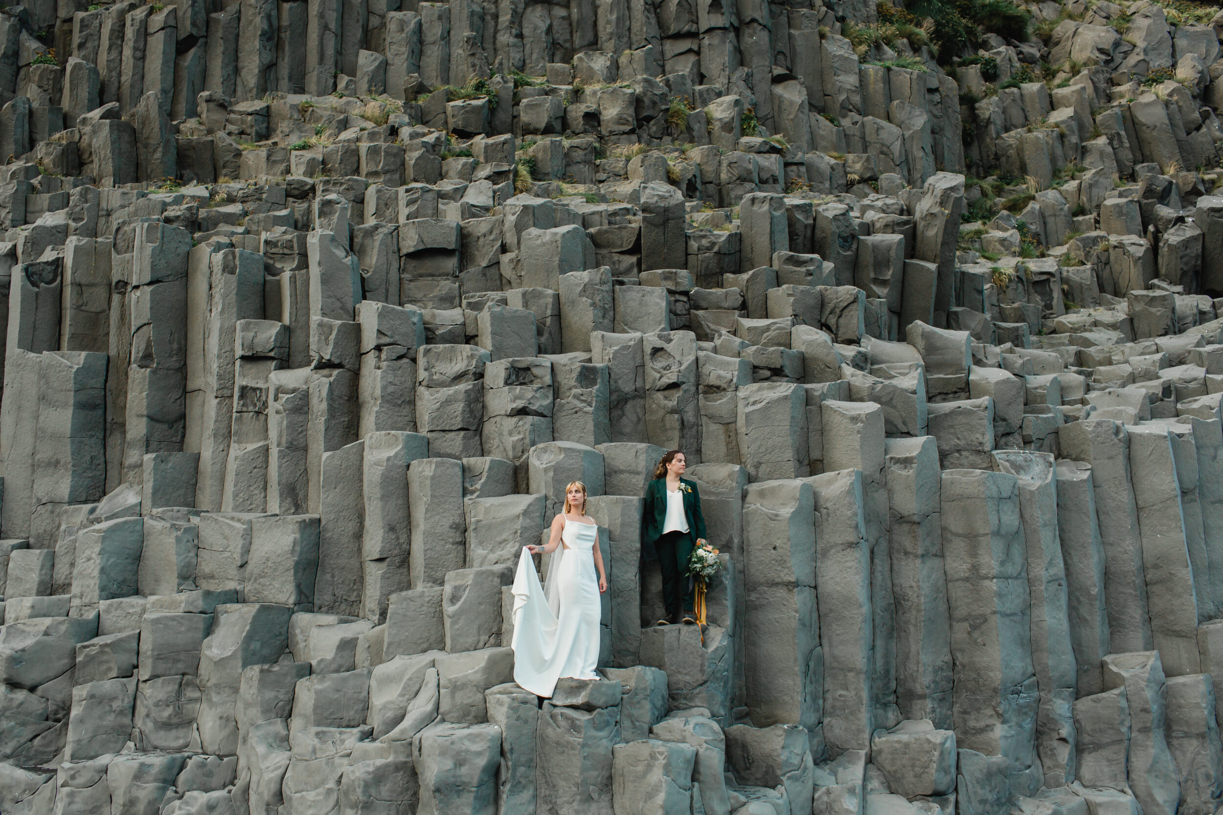 A woman and her wife stand on basalt columns in Iceland during their wedding portraits.