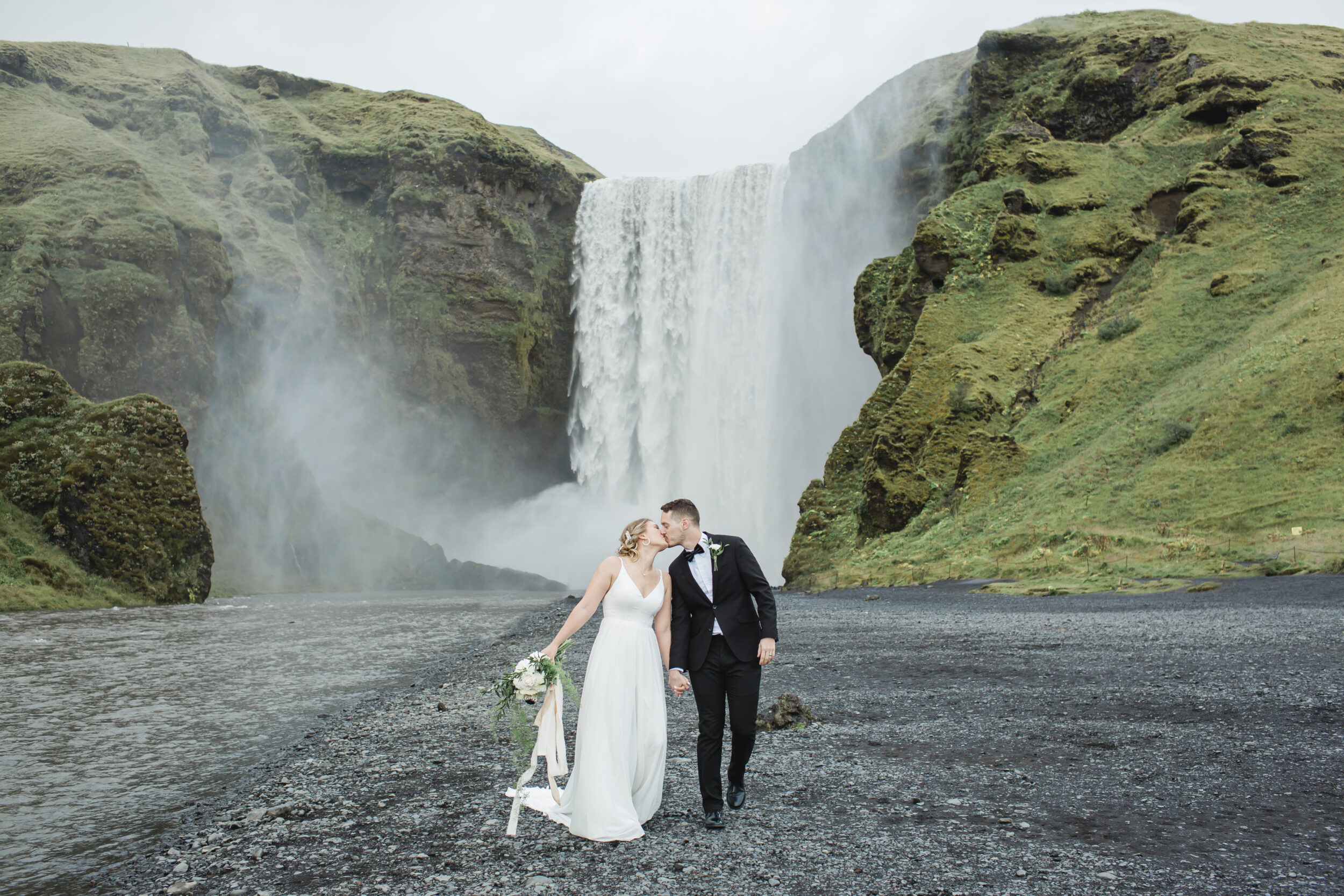 A couple is seen kissing near Skögafoss in wedding attire after their vow ceremony.
