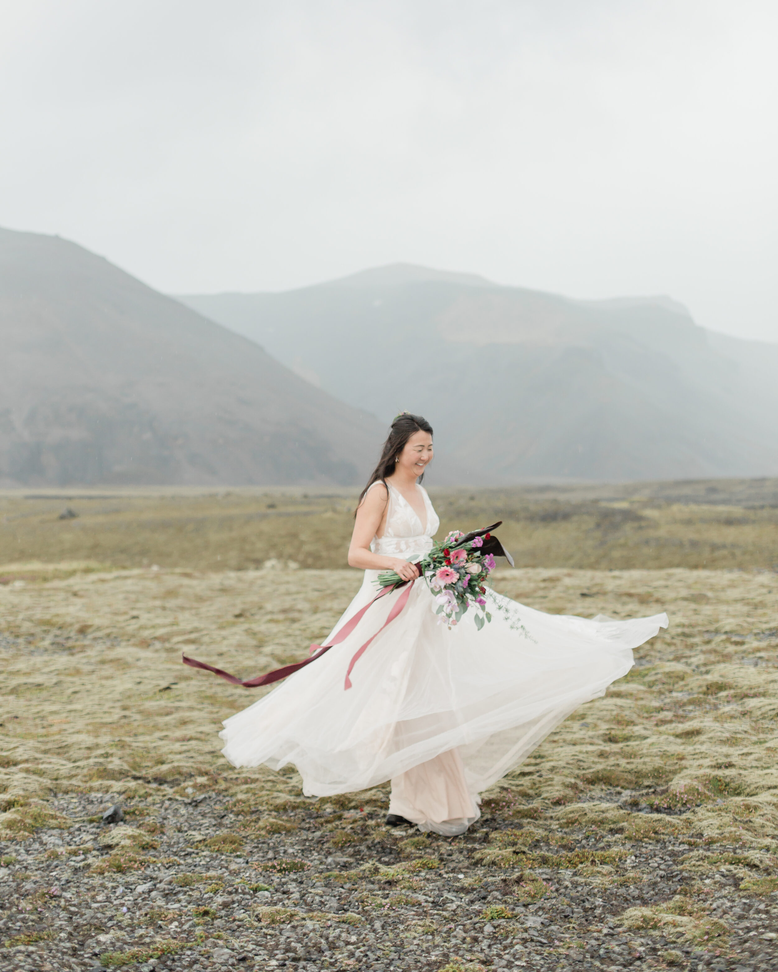 A bride twirls in her wedding dress in a field in Iceland.