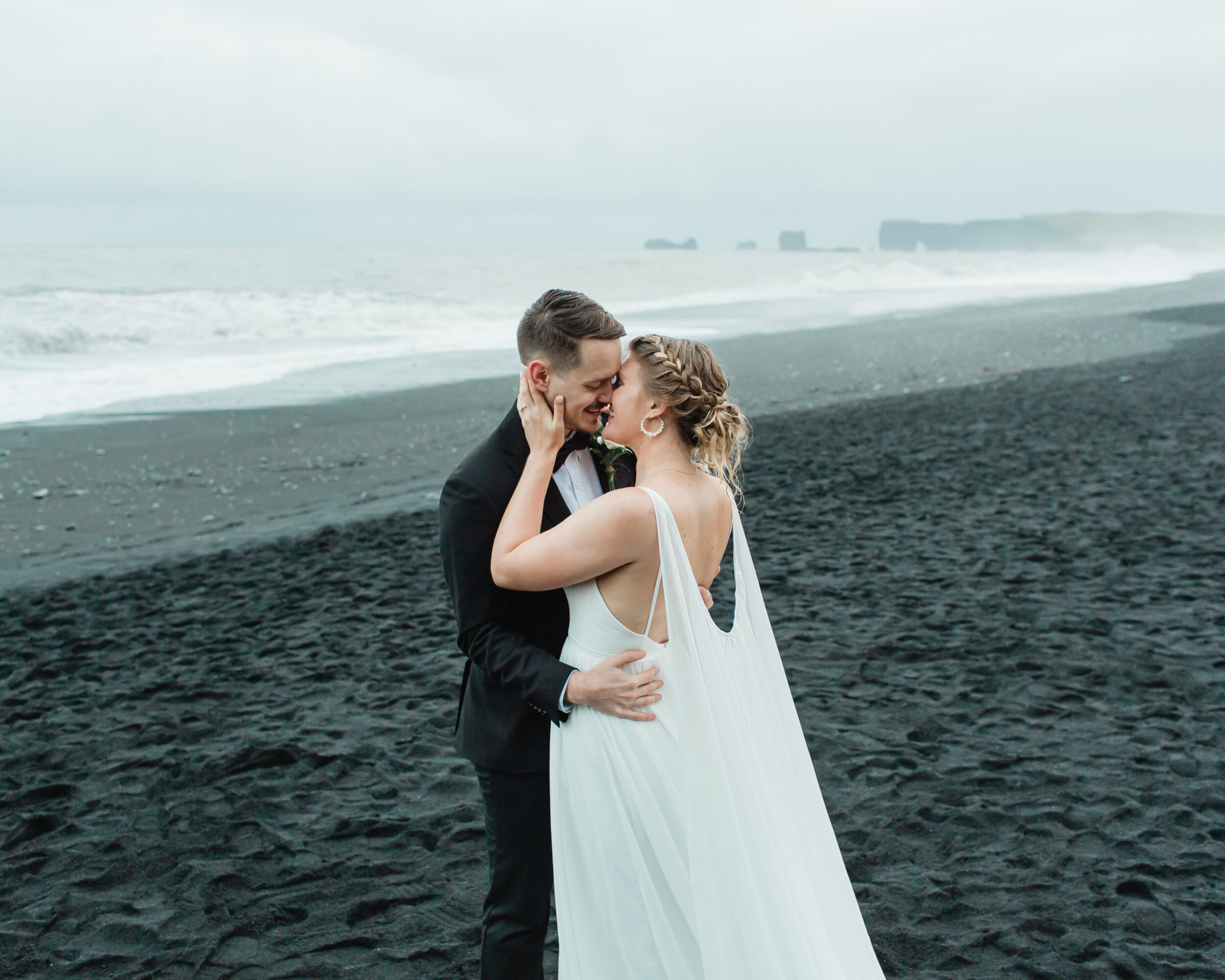 A bride goes into kiss her groom on a black, sandy beach in Southern Iceland.