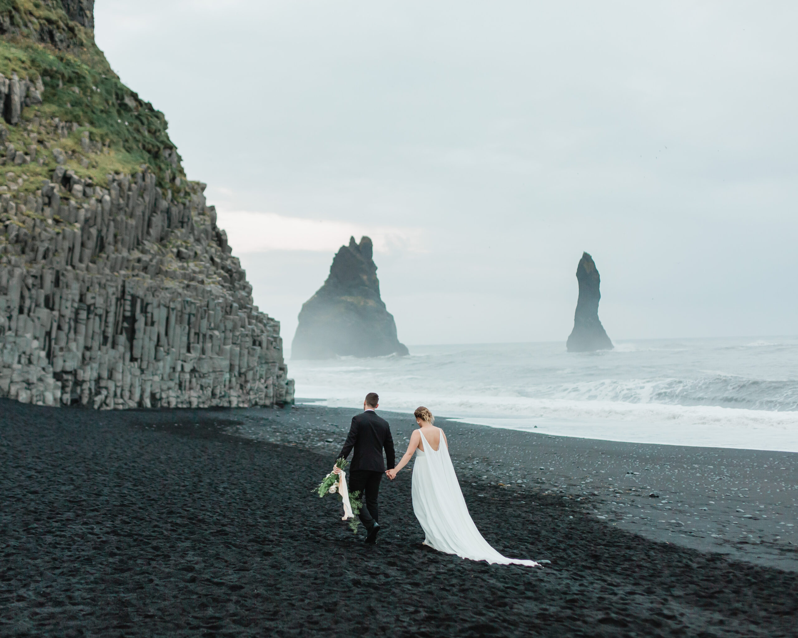A couple walks on a black sand beach in Iceland during their elopement.
