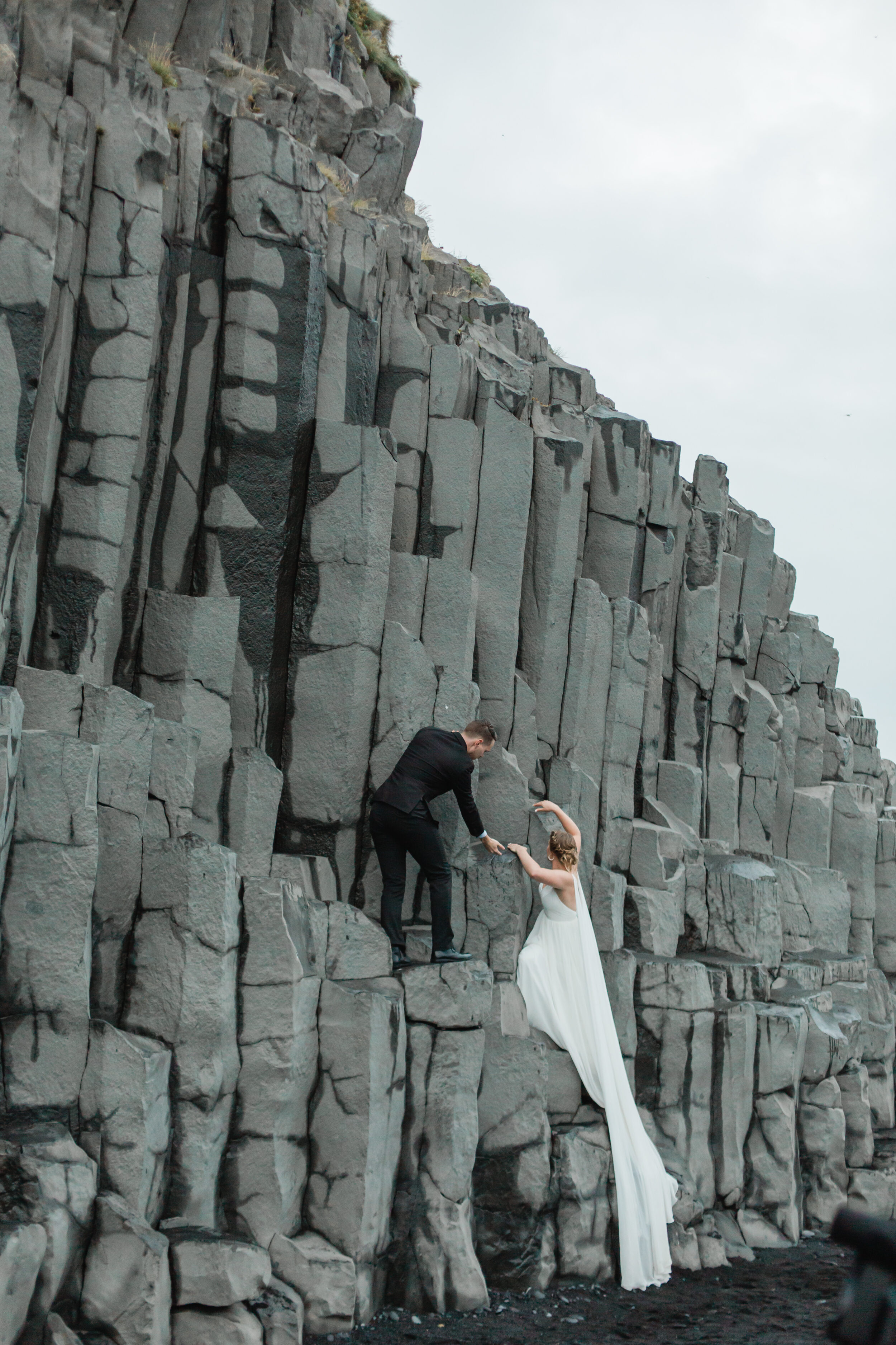 A groom helps his bride onto basalt columns in Iceland.