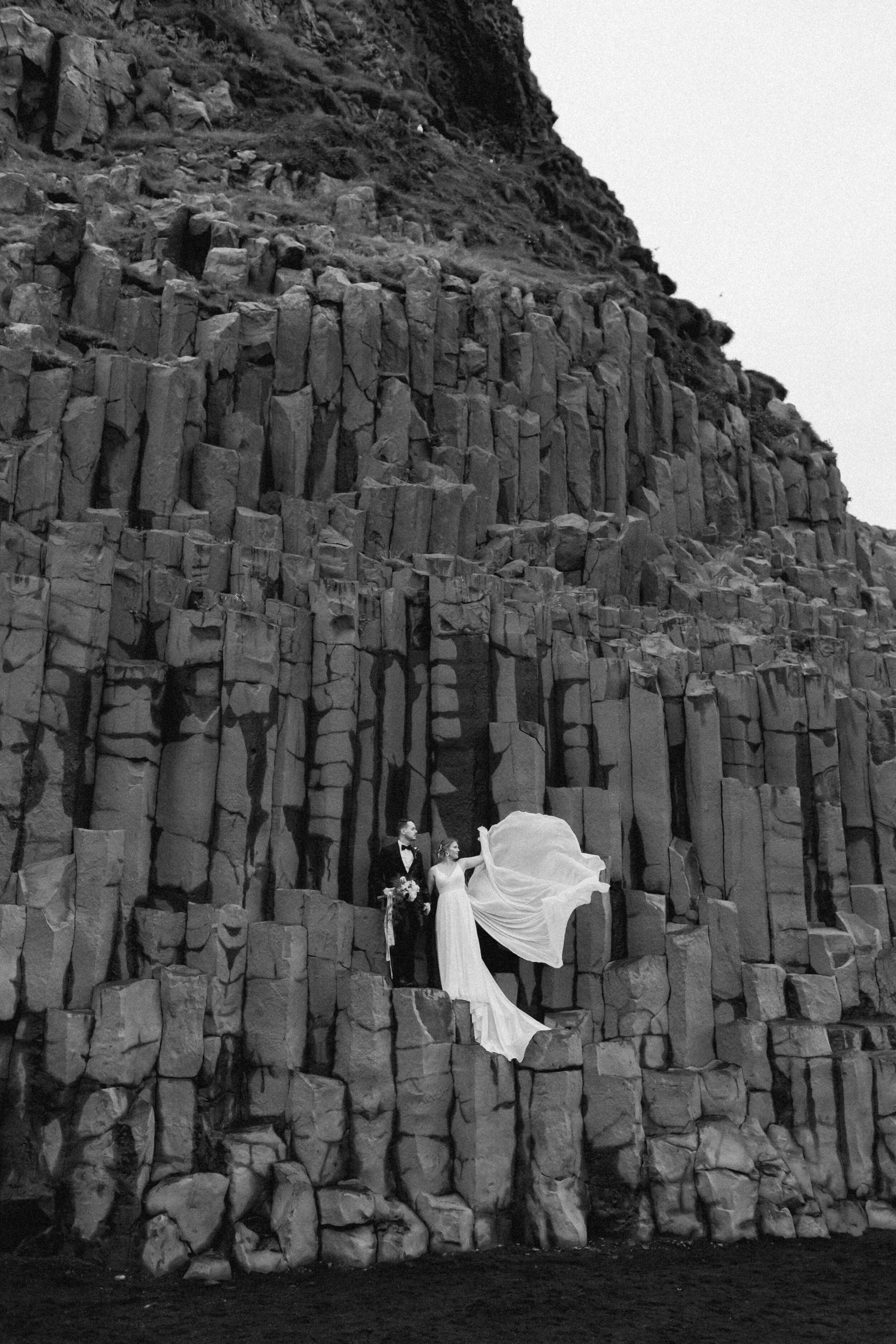 A couple stands on basalt columns during their Iceland wedding.