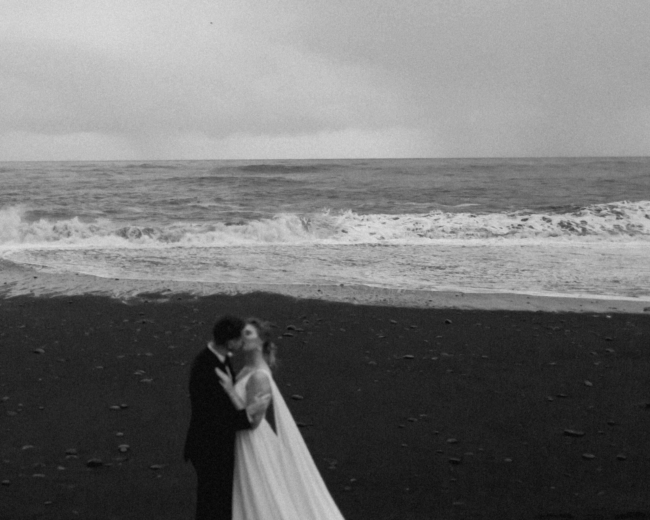 A couple embraces while on the shores of a black sand beach in Southern Iceland