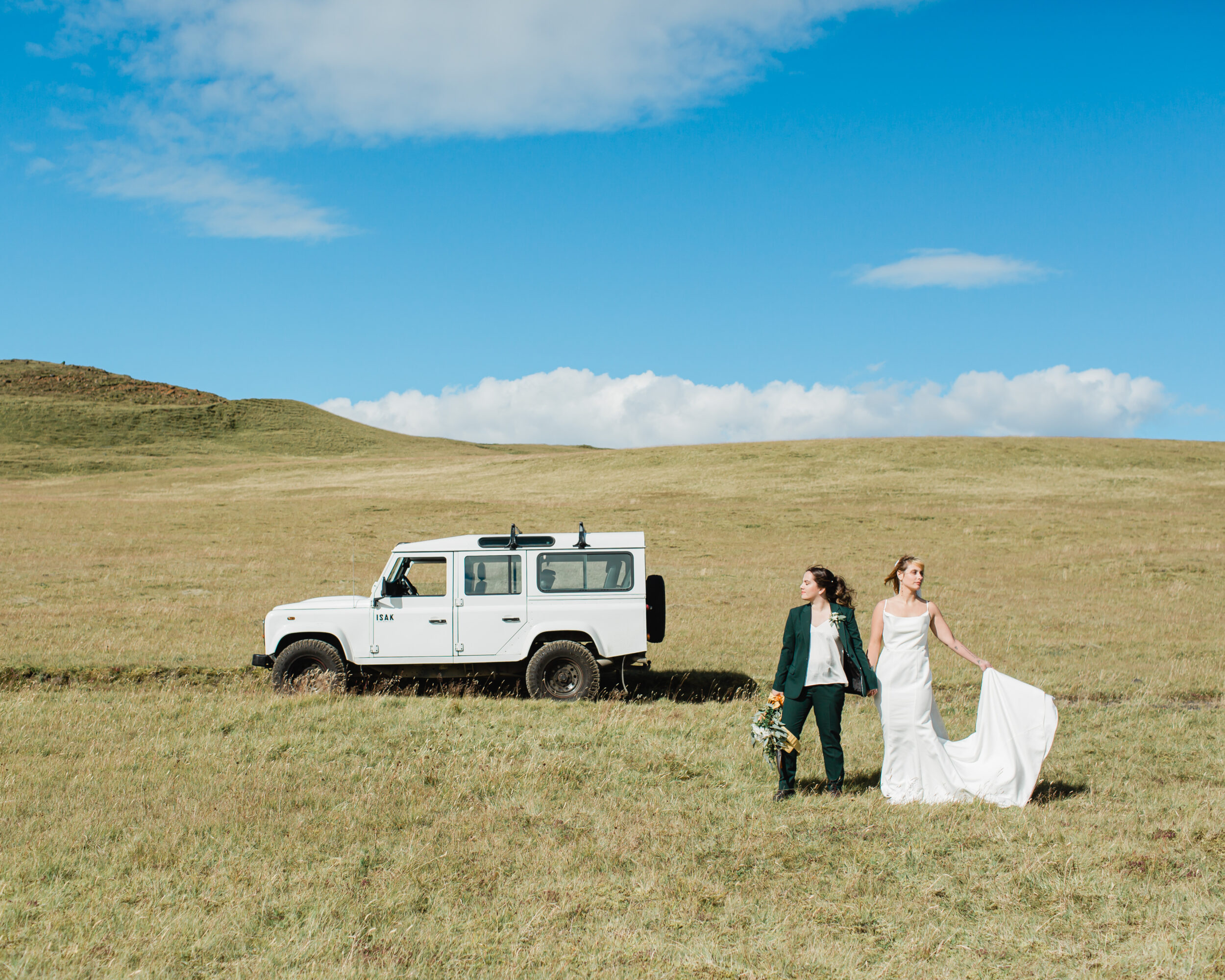 A couple stands in a grassy meadow in Iceland next to a 4x4 vehicle.