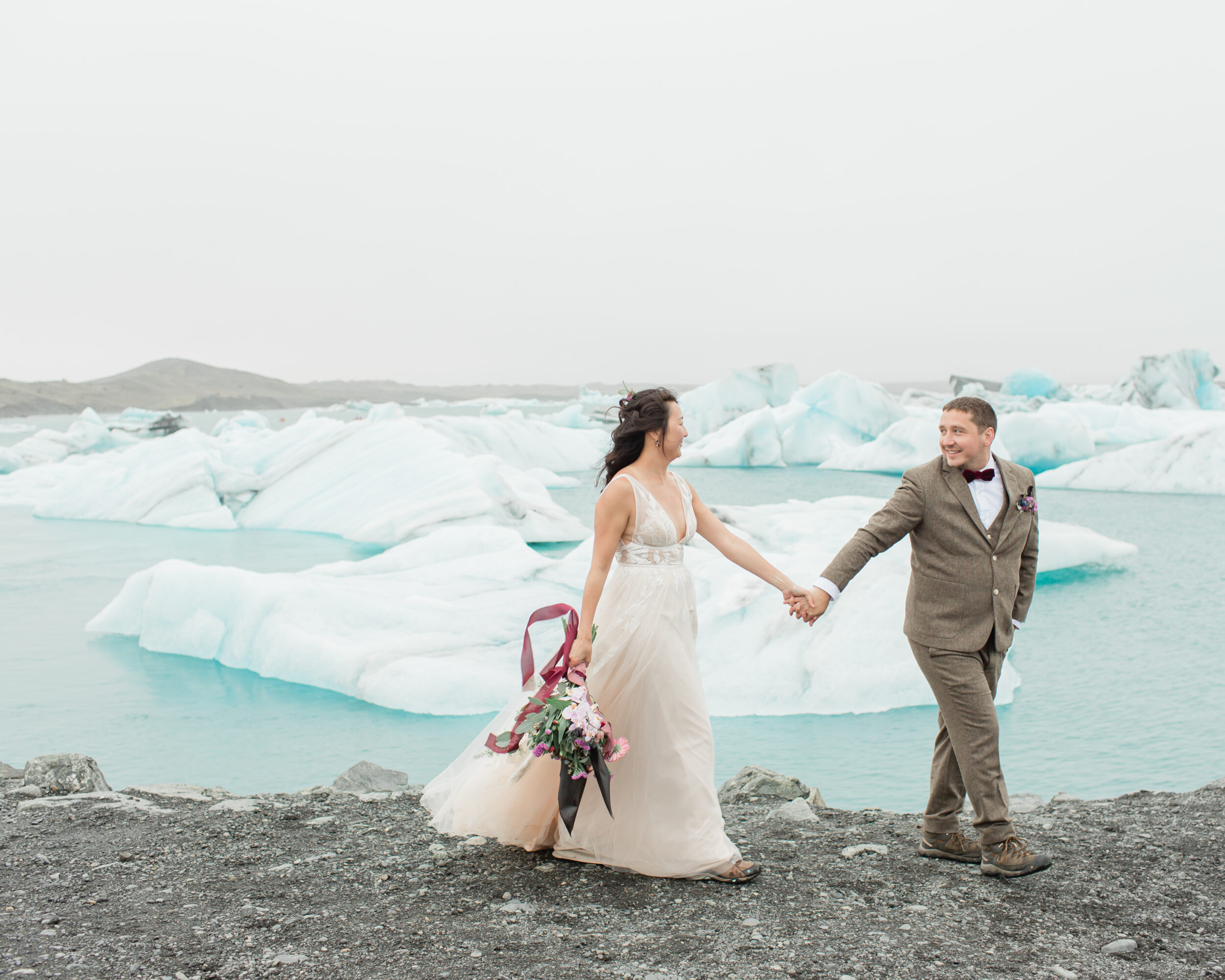 A couple walks hand in hand wearing elopement attire in Iceland.