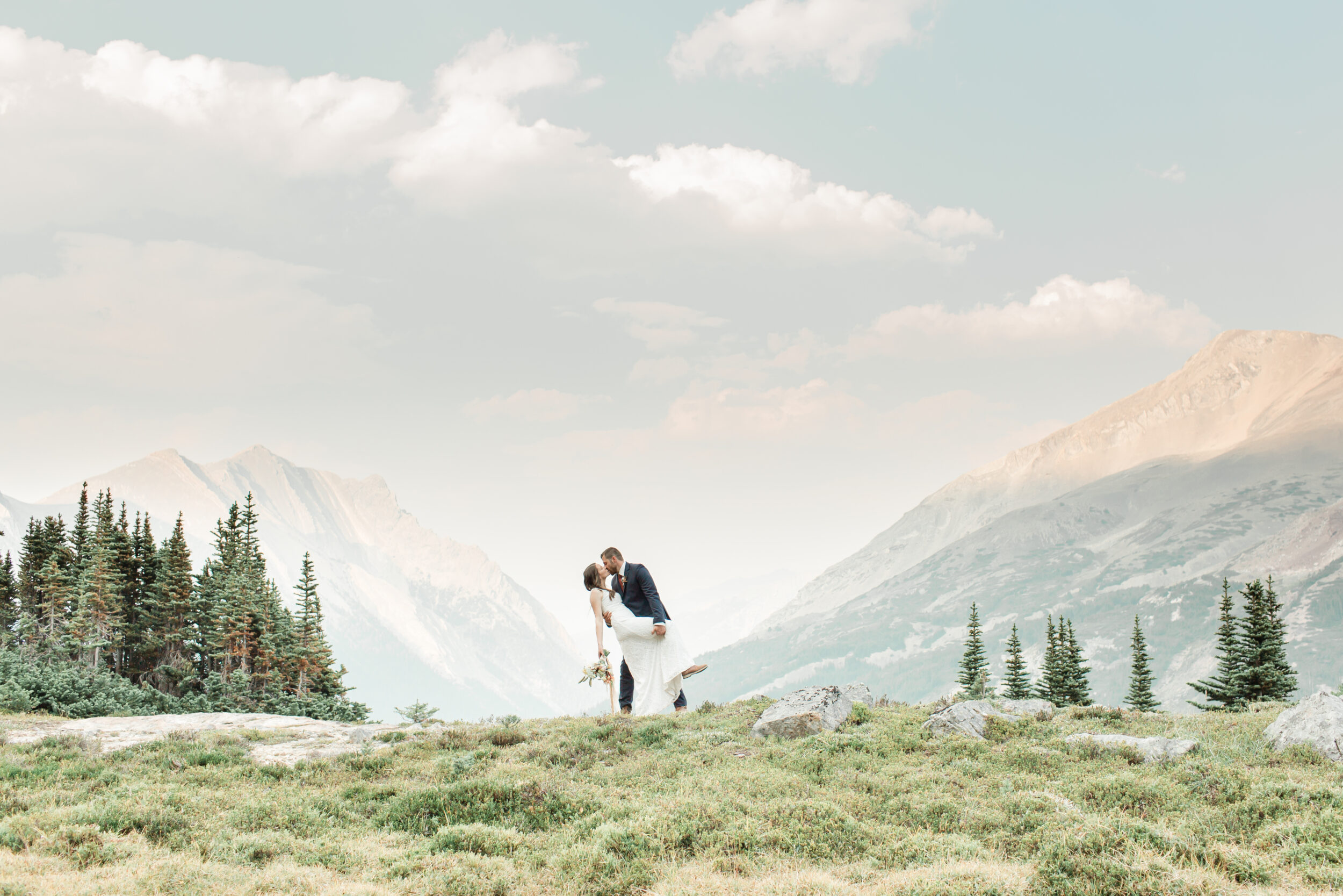 A man and woman share a kiss against a beautiful mountain backdrop.