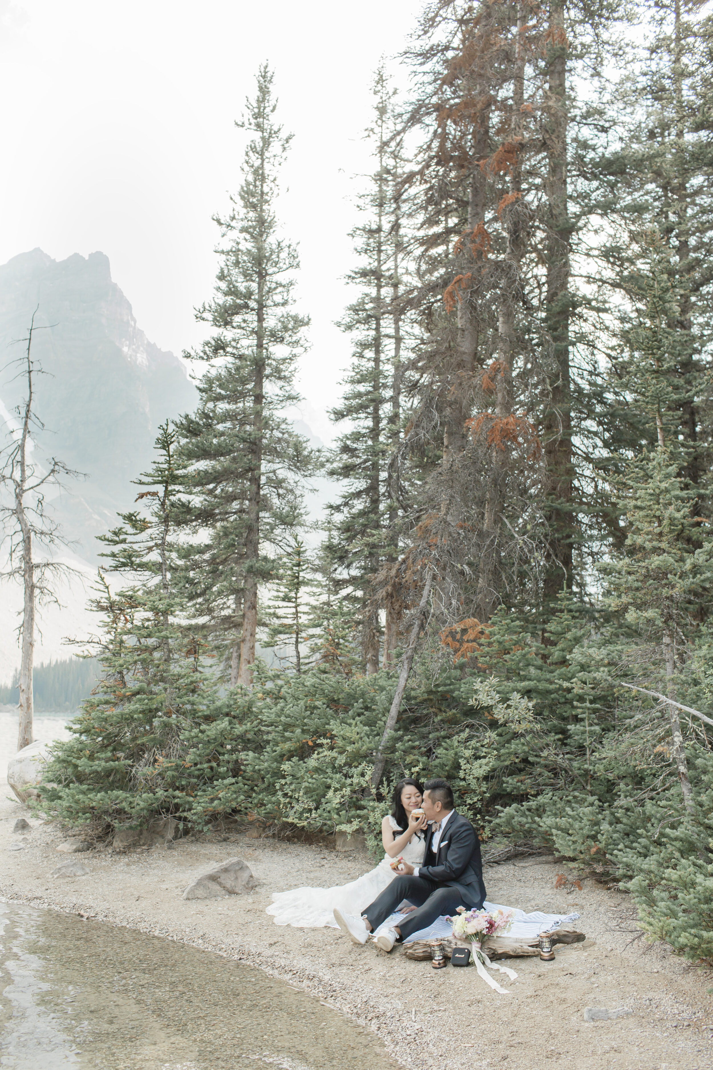 A newlywed couple shares a picnic on an alpine lake.