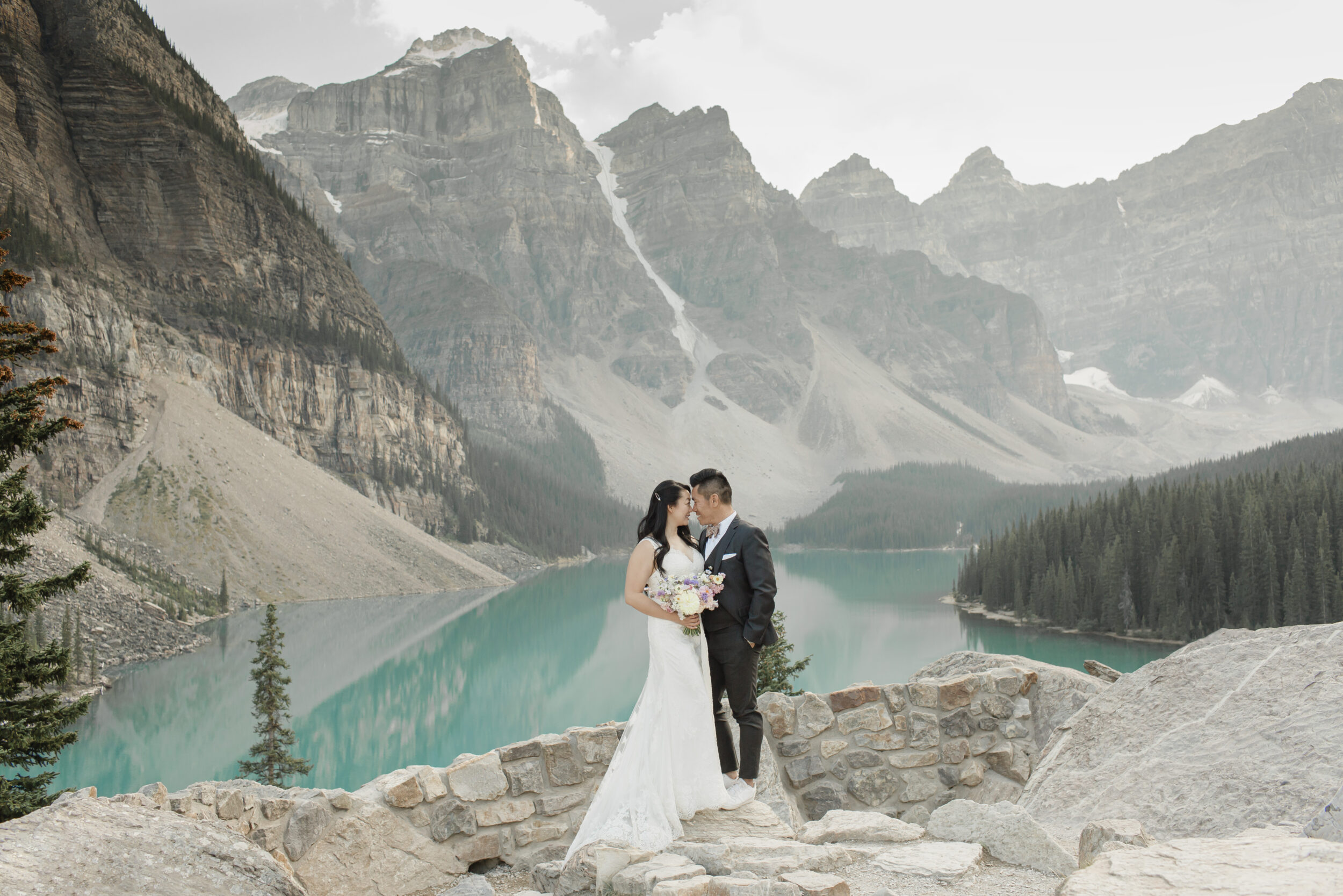 A couple stands in wedding attire near an alpine lake in Banff.