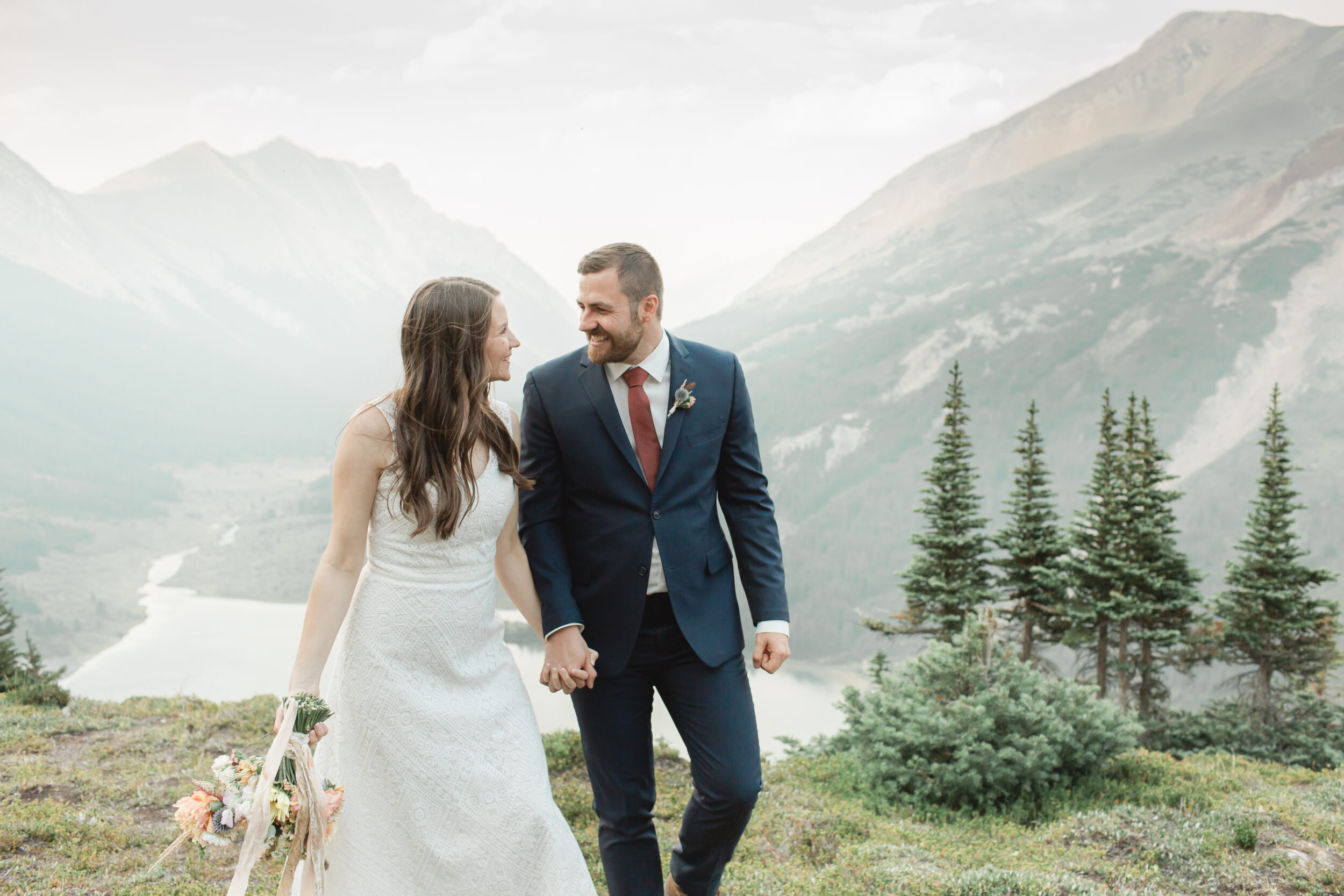 A couple walks in Banff National Park and holds hands after their outdoor wedding.
