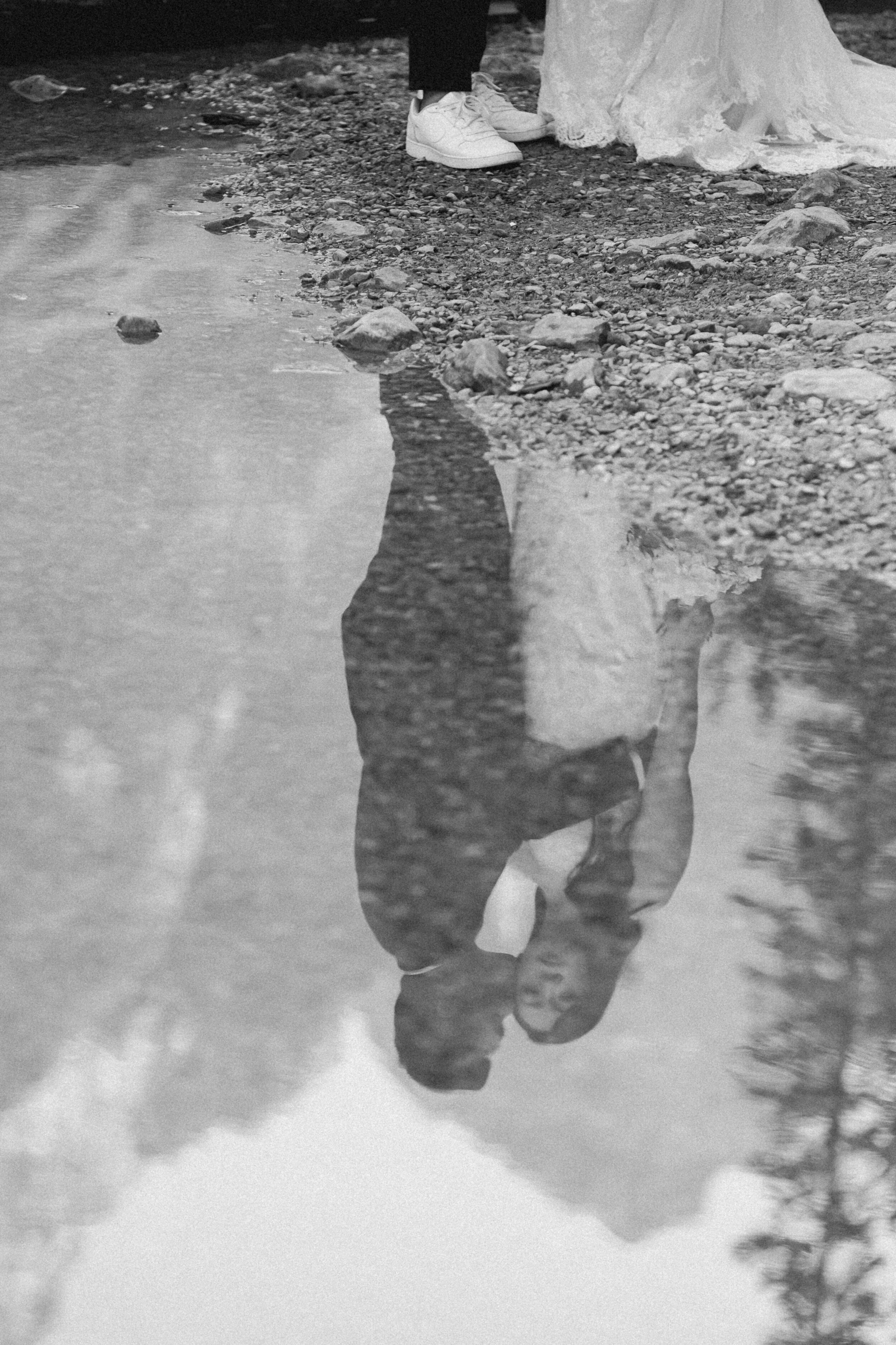 A couple's reflection is shown in an alpine lake's reflection.