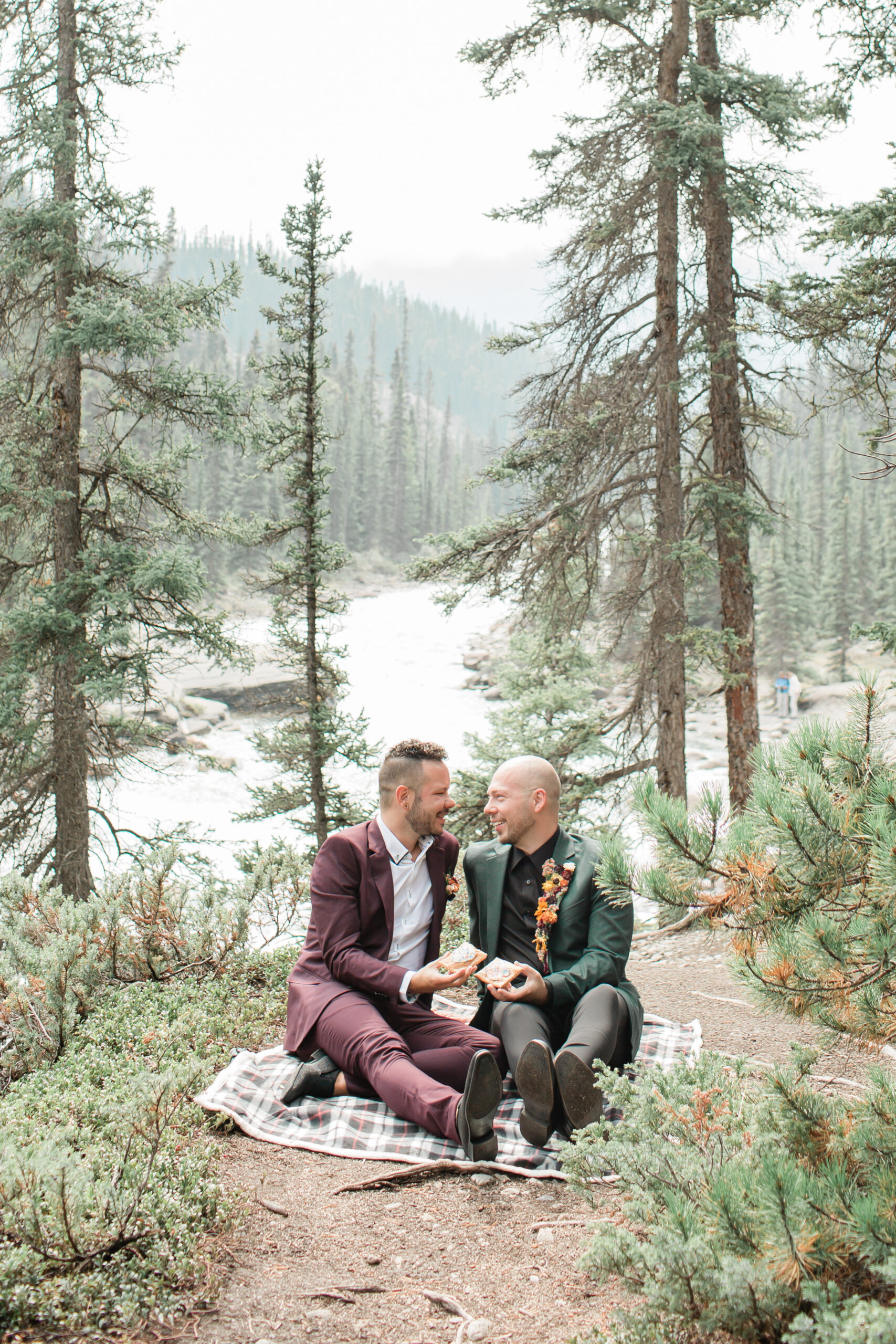 Newlyweds sit on a picnic blanket and celebrate their Banff National Park elopement.
