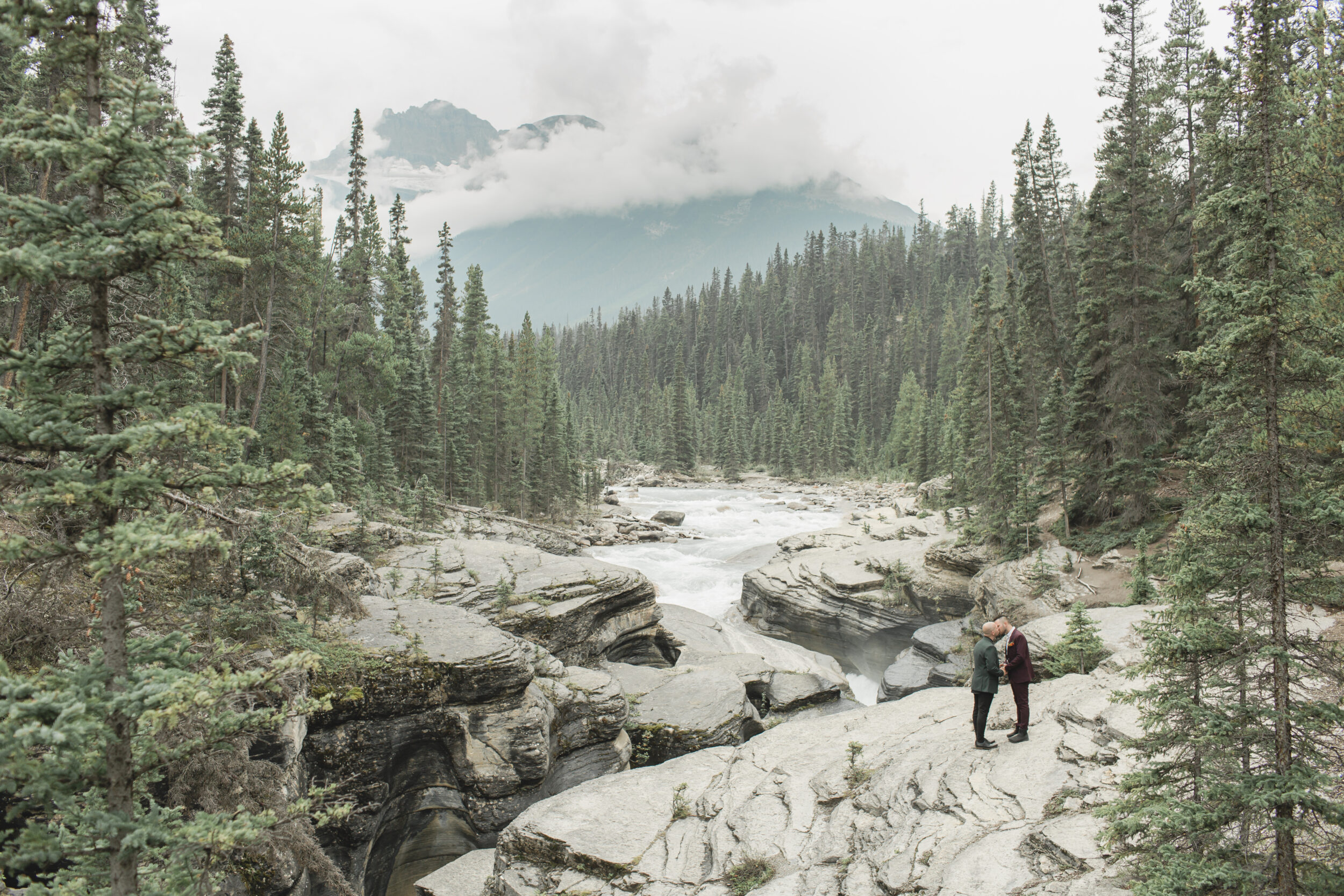 A couple holds hands on a river overlook in Banff National Park during their elopement.