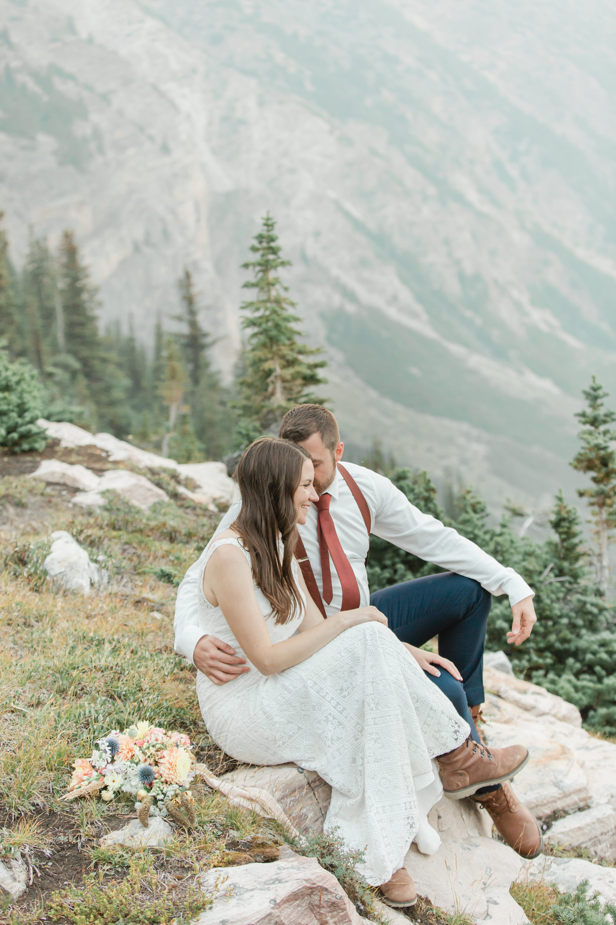 A newly married couple embraces while sitting on a mountainside in Banff.