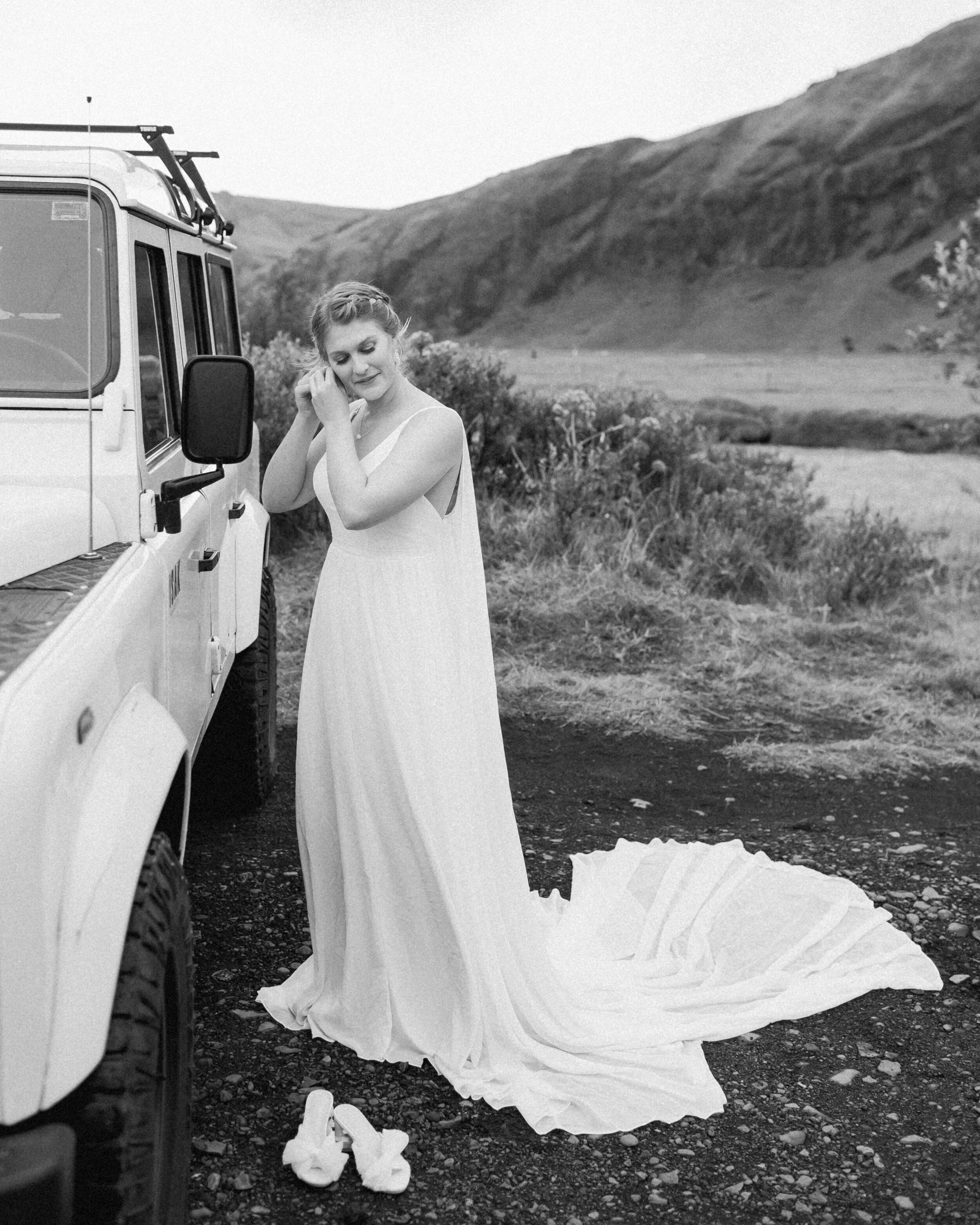 A woman puts on earrings near a 4x4 before her Iceland elopement. 