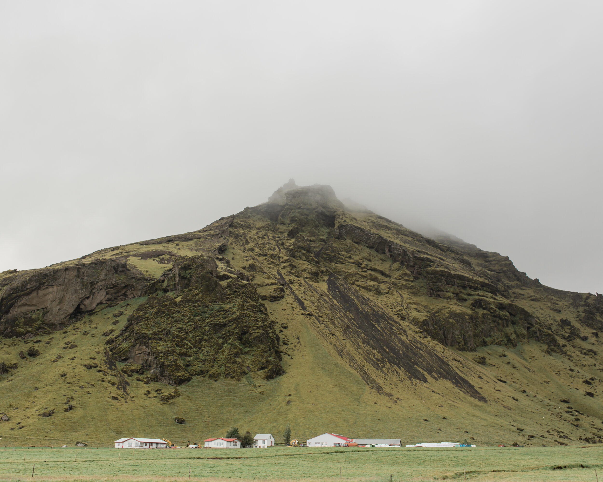 A foggy Icelandic mountain peak towers over a small town.