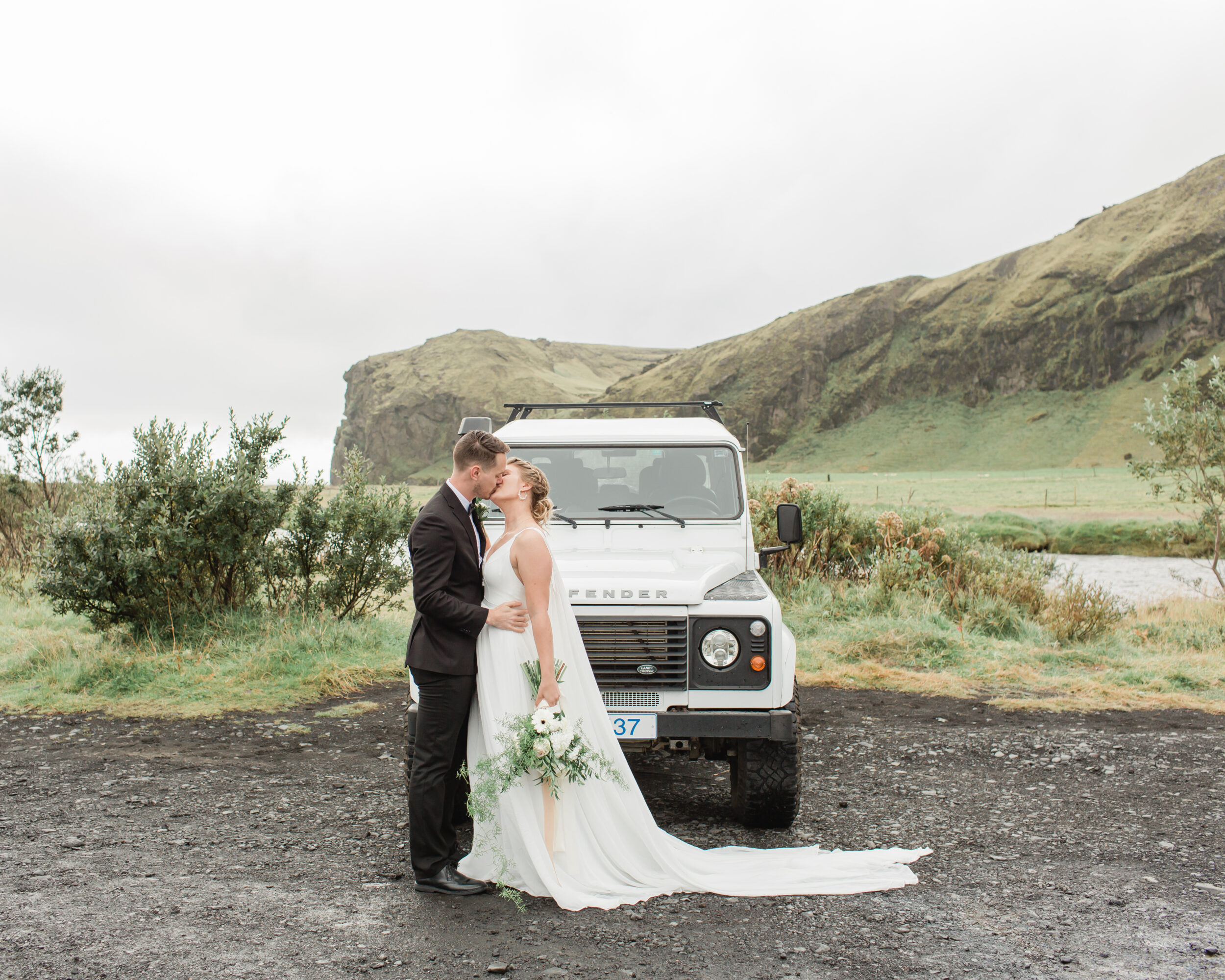 A couple kisses in front of a Defender during their Skogafoss wedding ceremony. 