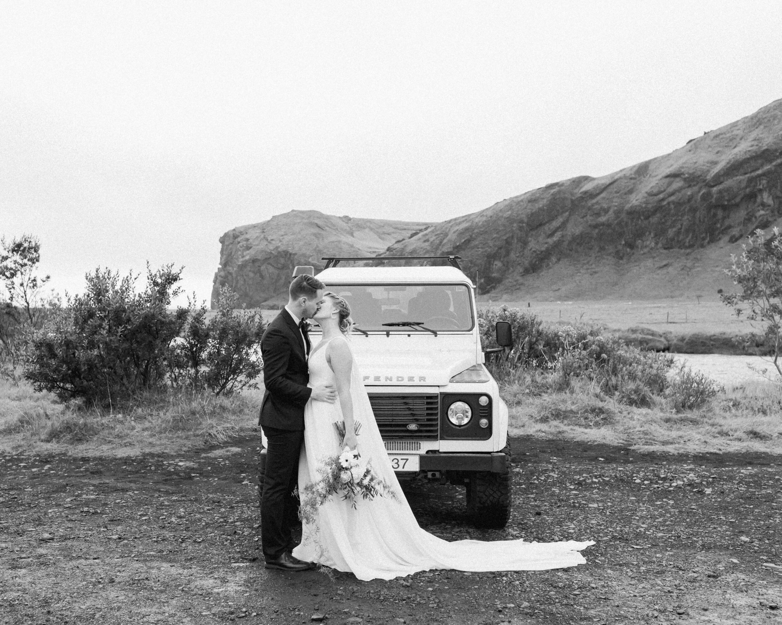 A couple kisses in front of an off-roading vehicle in Iceland. 