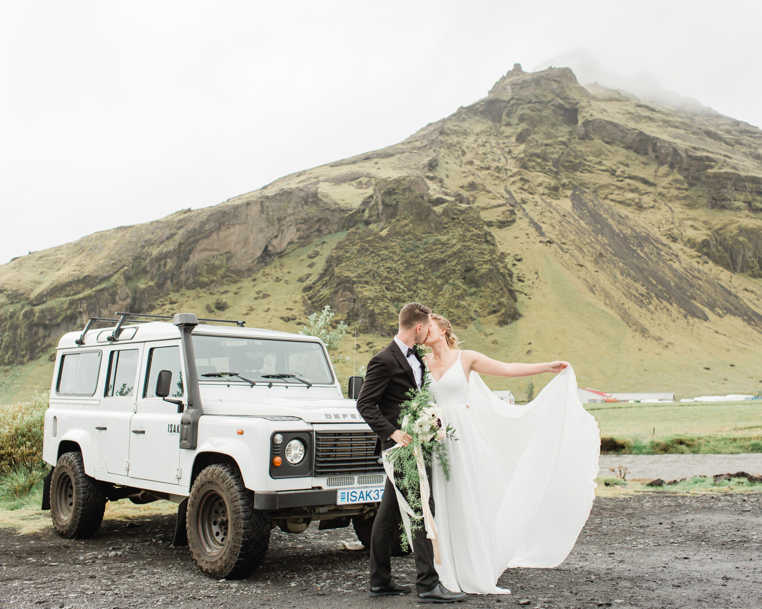 A bride displays her white wedding dress while kissing her groom during their Skogafoss adventure elopement. 