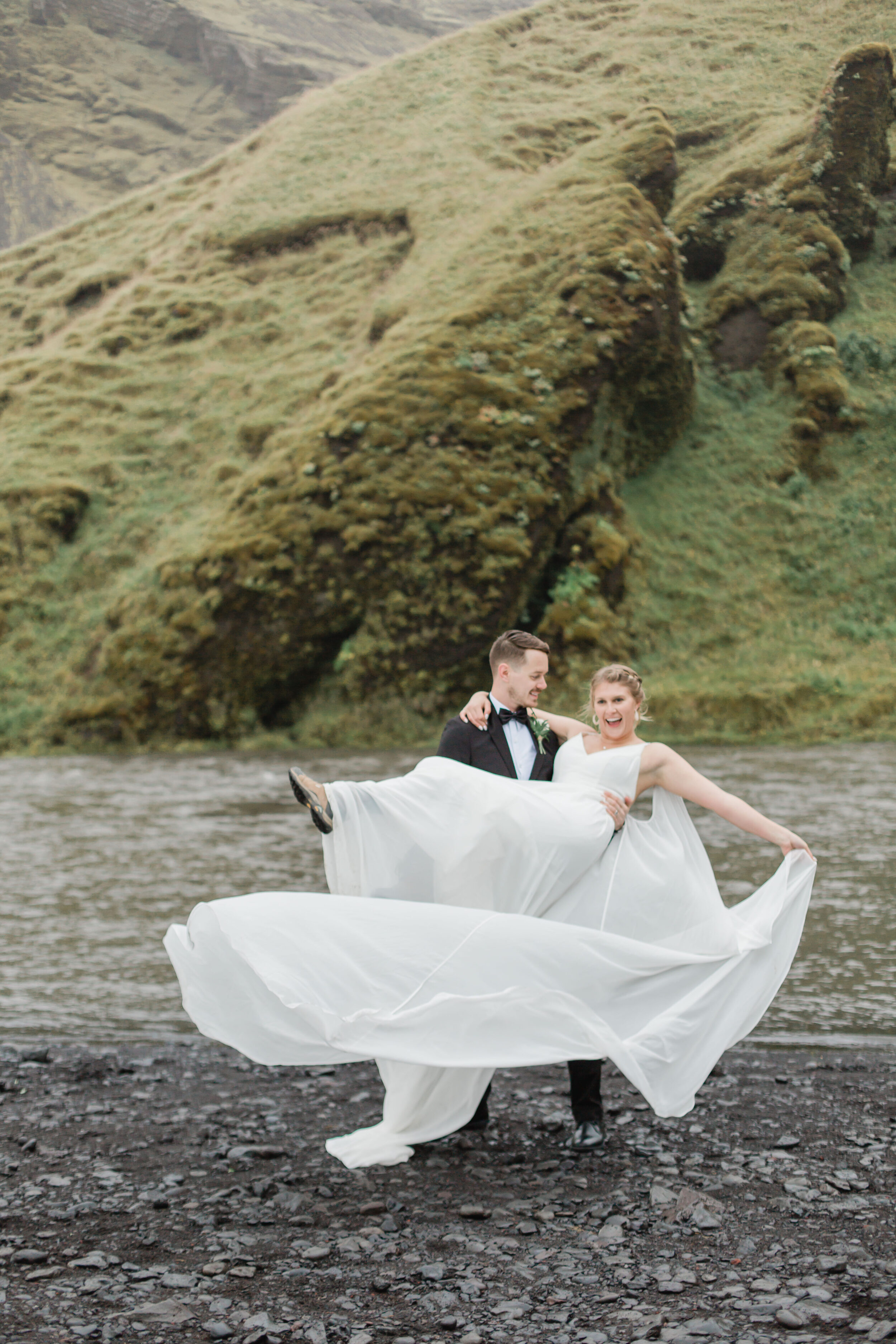 A man holds his bride near a Icelandic stream at Skogafoss.