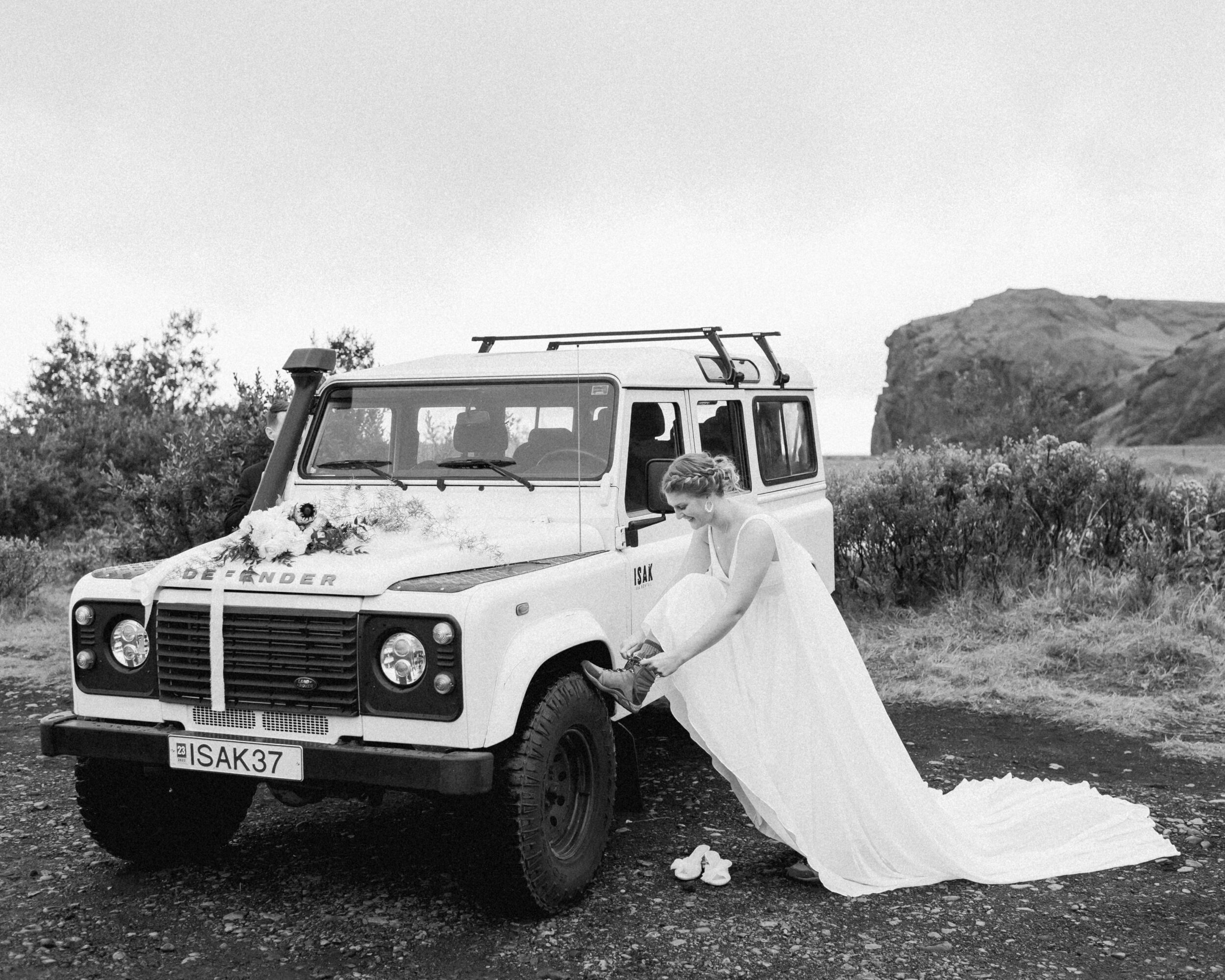 A bride rests her hiking boots on her Defender while tying her shoes. 