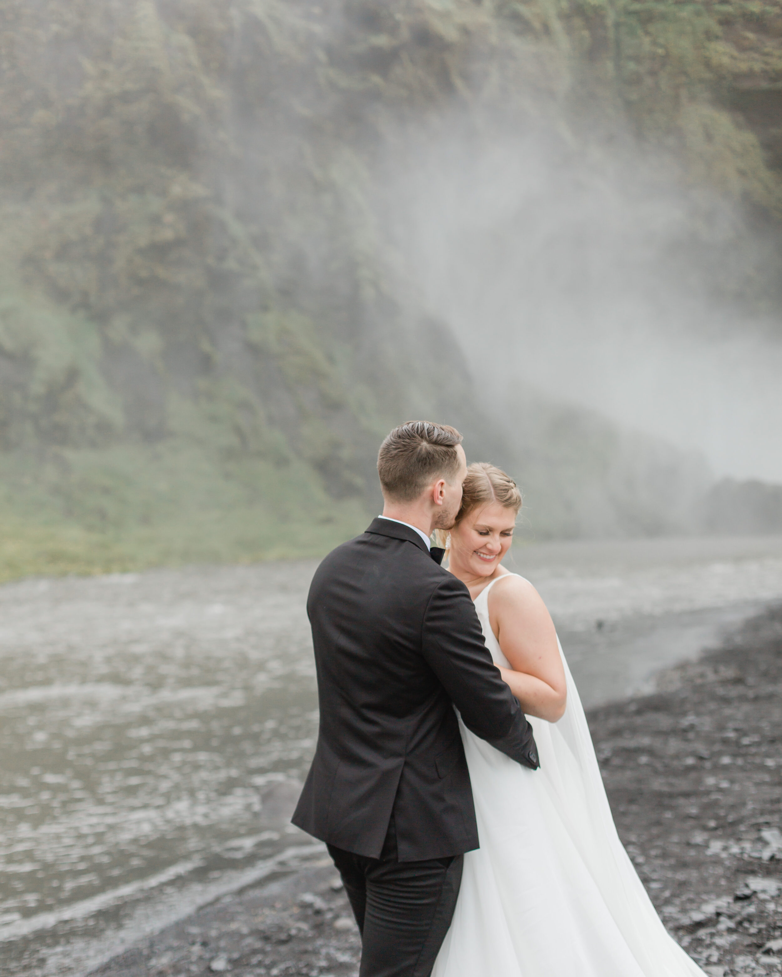A groom kisses his brides forehead near a chilly Icelandic stream.