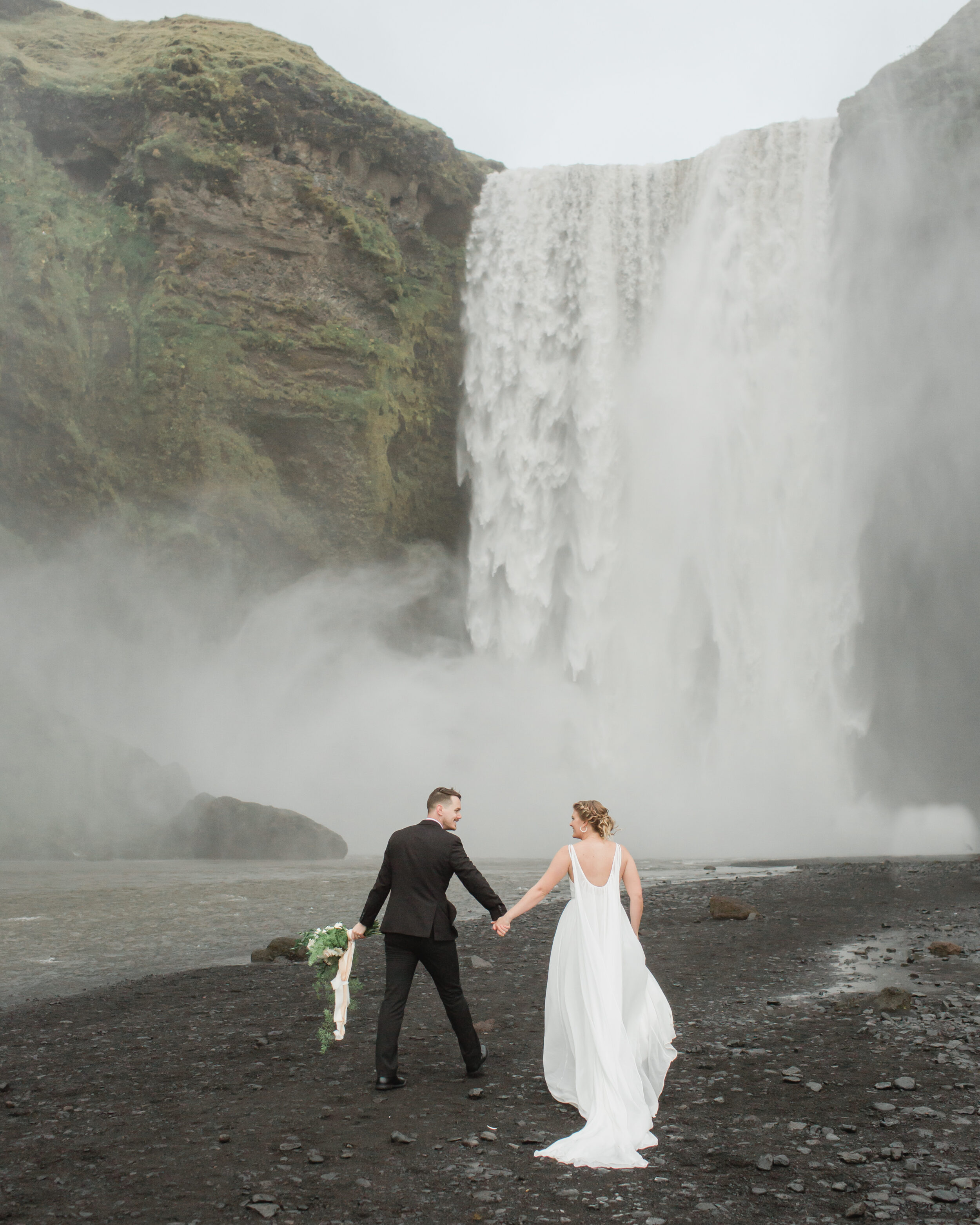 A couple walks towards a large waterfall in Iceland during their wedding ceremony. 