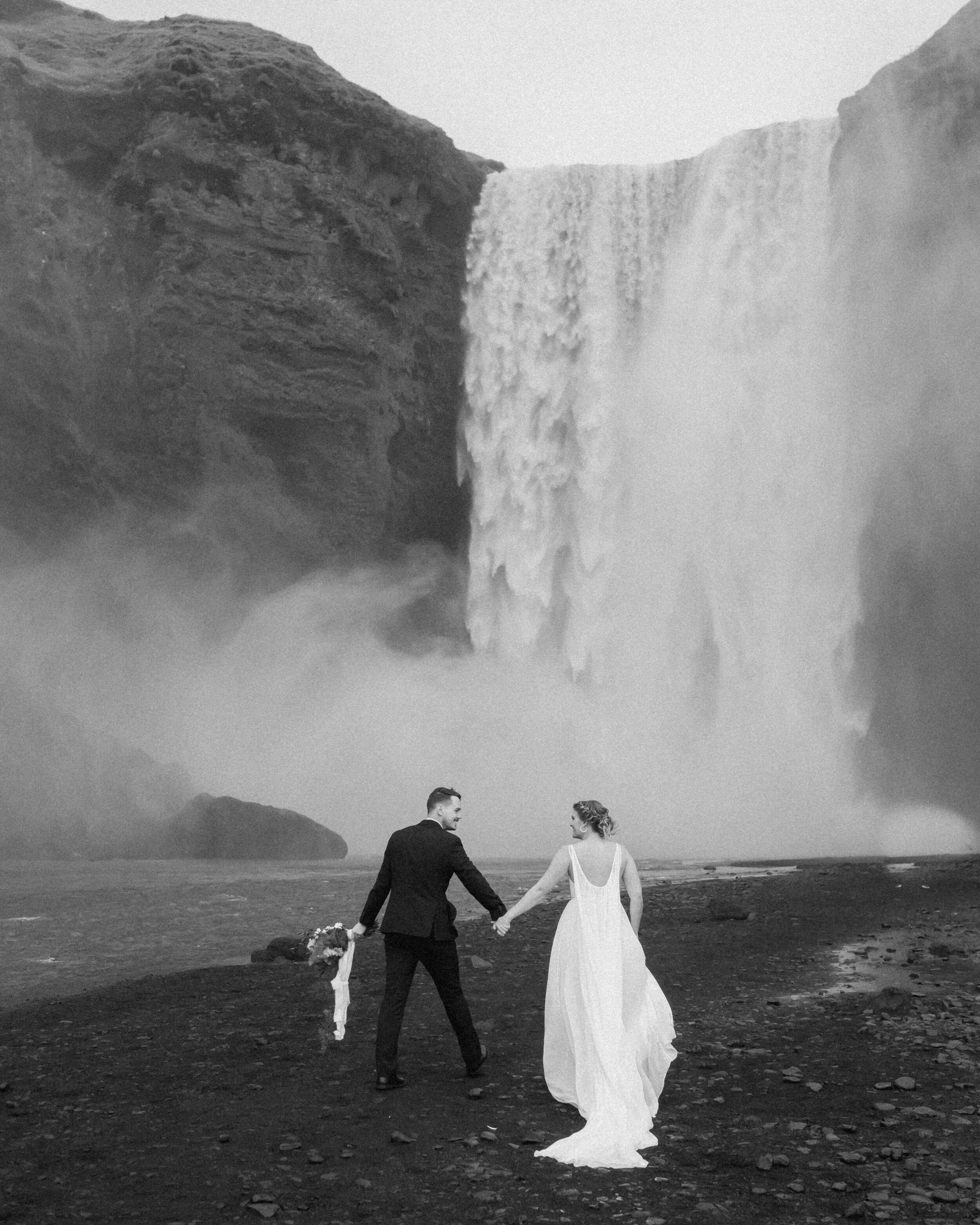 A couple walks hand in hand before saying their elopement vows at Skogafoss.