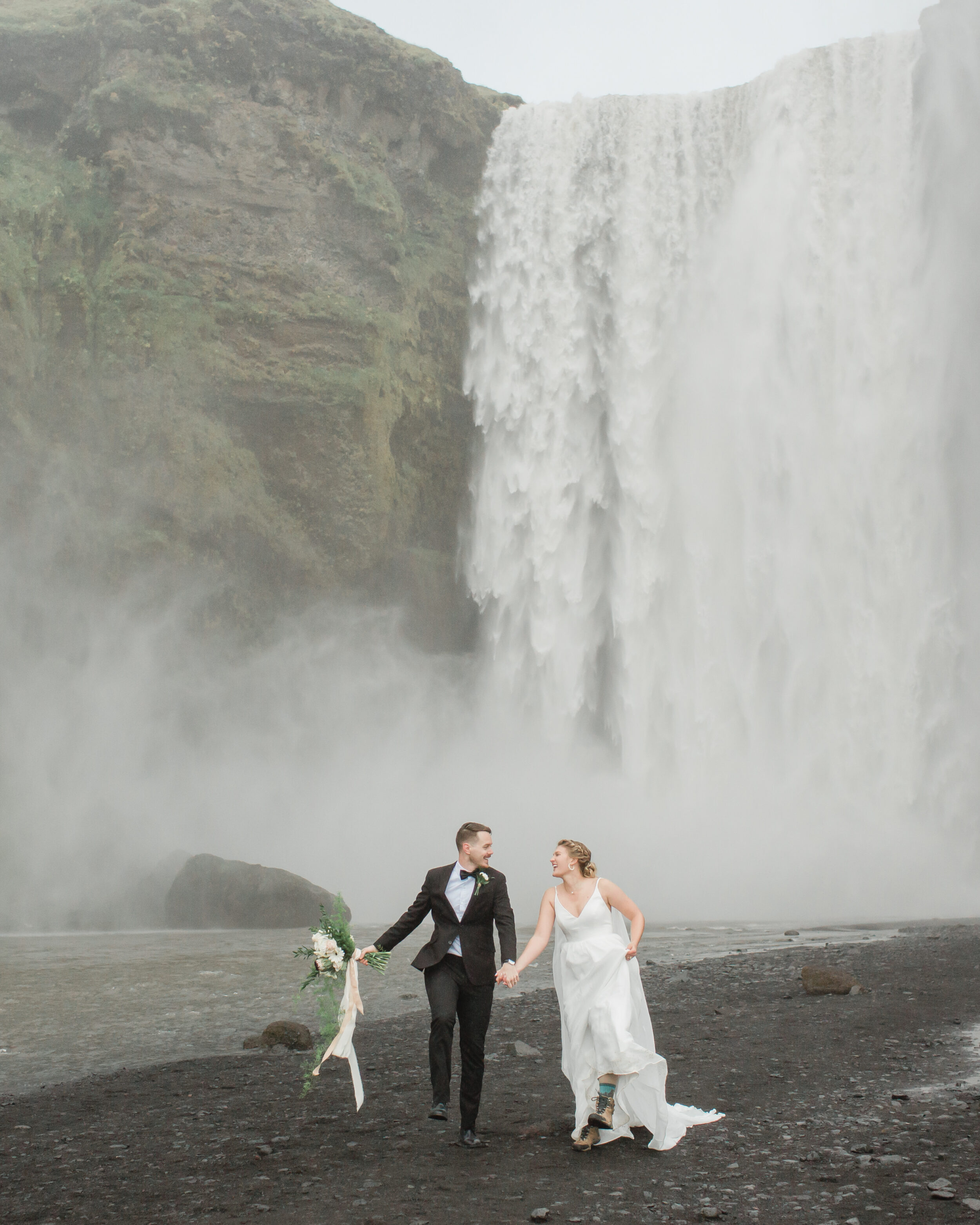 A couple skips on the rocks in front of Skogafoss during their elopement. 