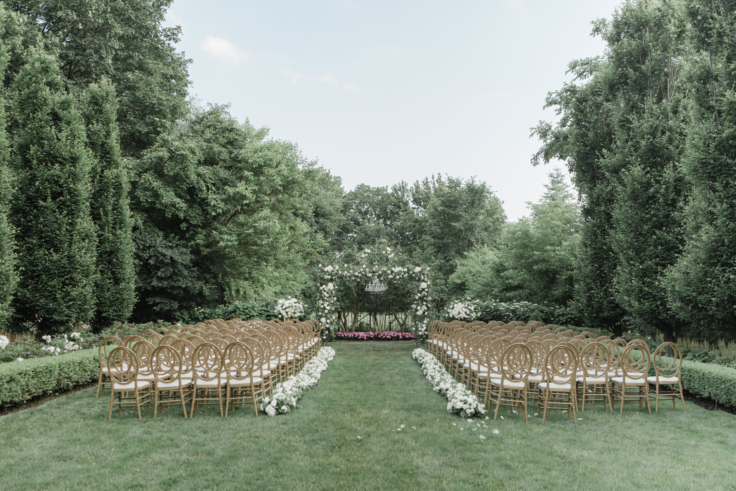 A beautiful outdoor wedding in Toronto with a floral arch is seen amongst trees.