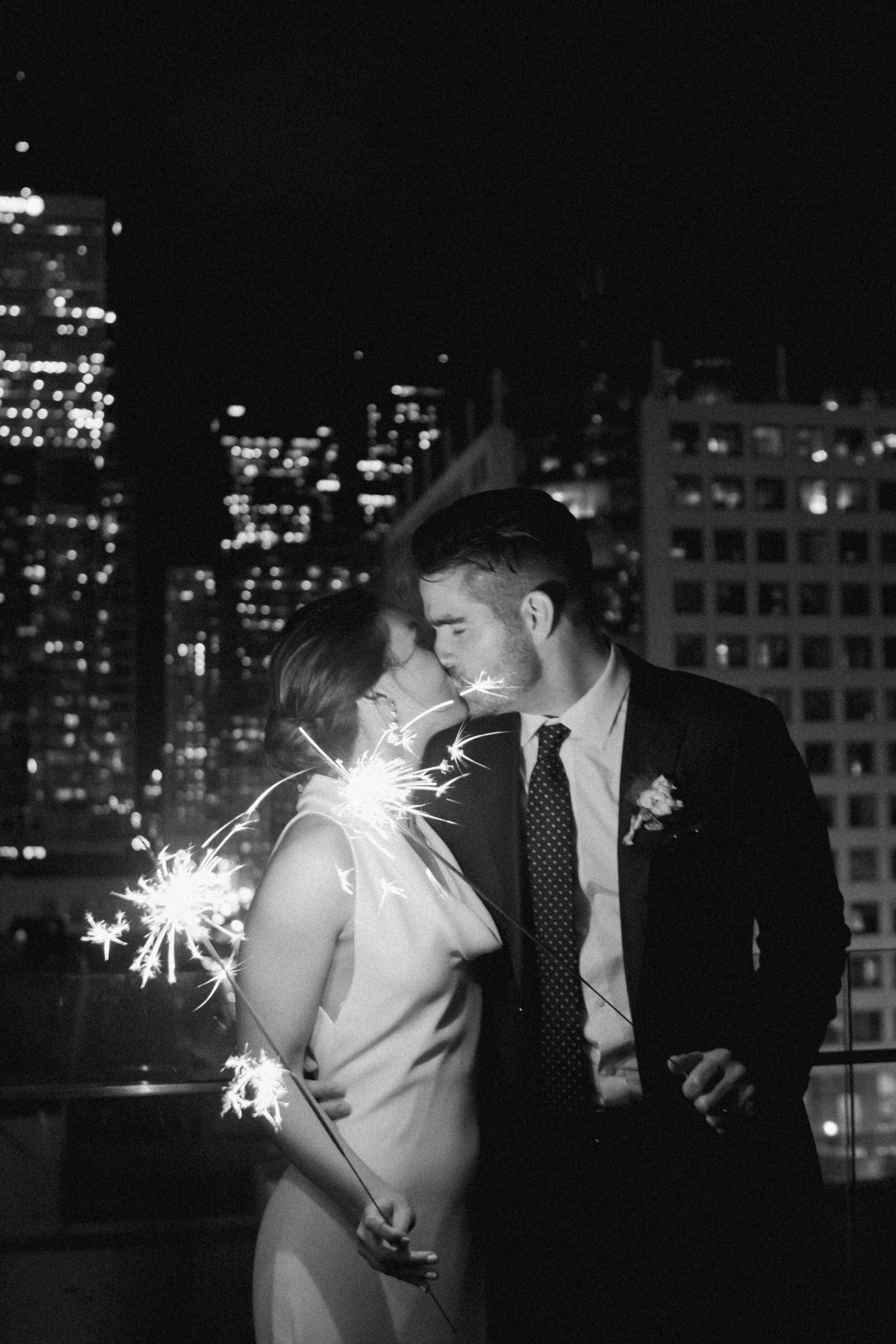 A newlywed couple kisses after their wedding in Toronto with a sparkler lit in hand. 