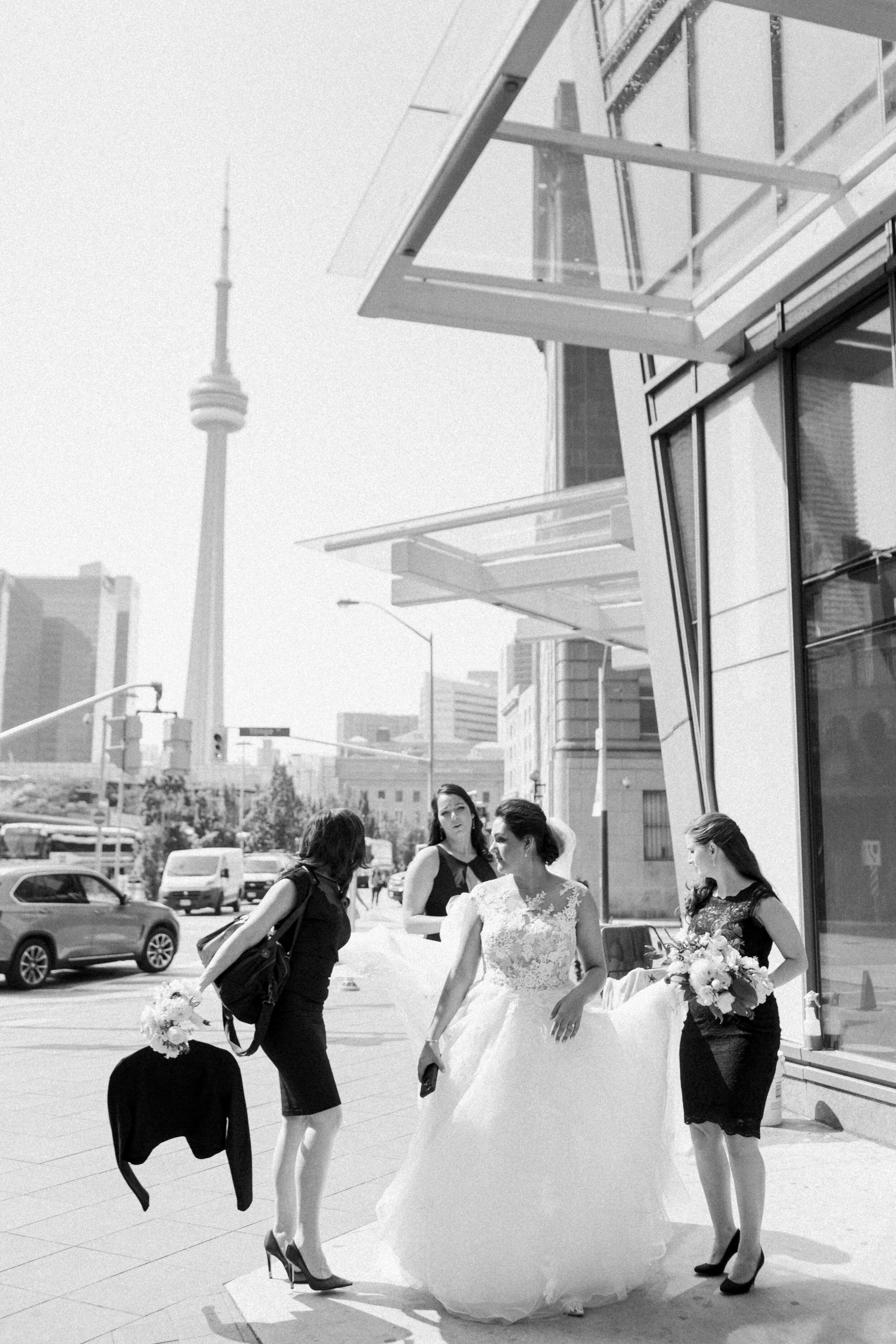A woman in a wedding dress is seen walking in the streets of Toronto with the CN Tower in the background. 