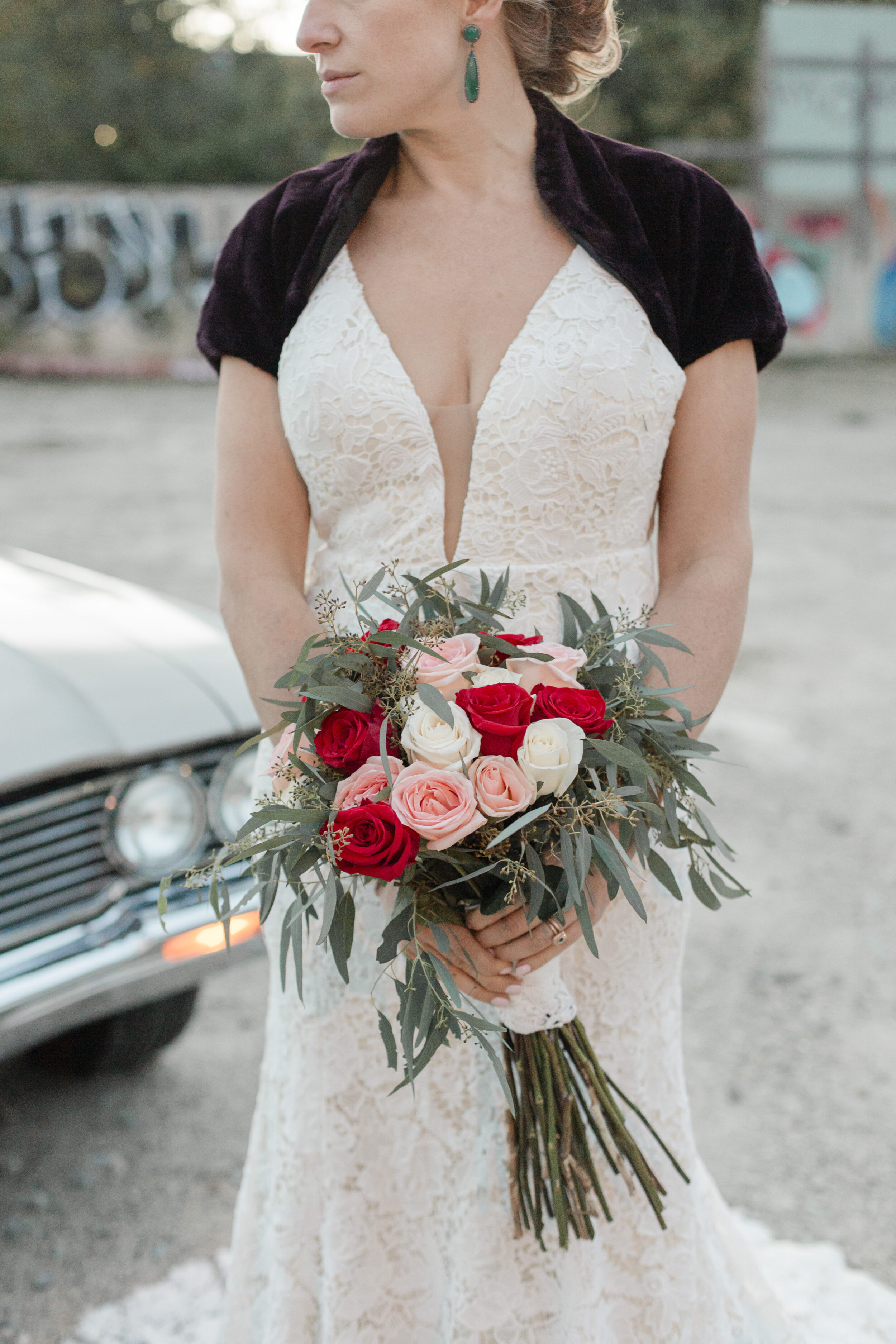 A bride holds a red, white and pink rose floral bridal bouquet.