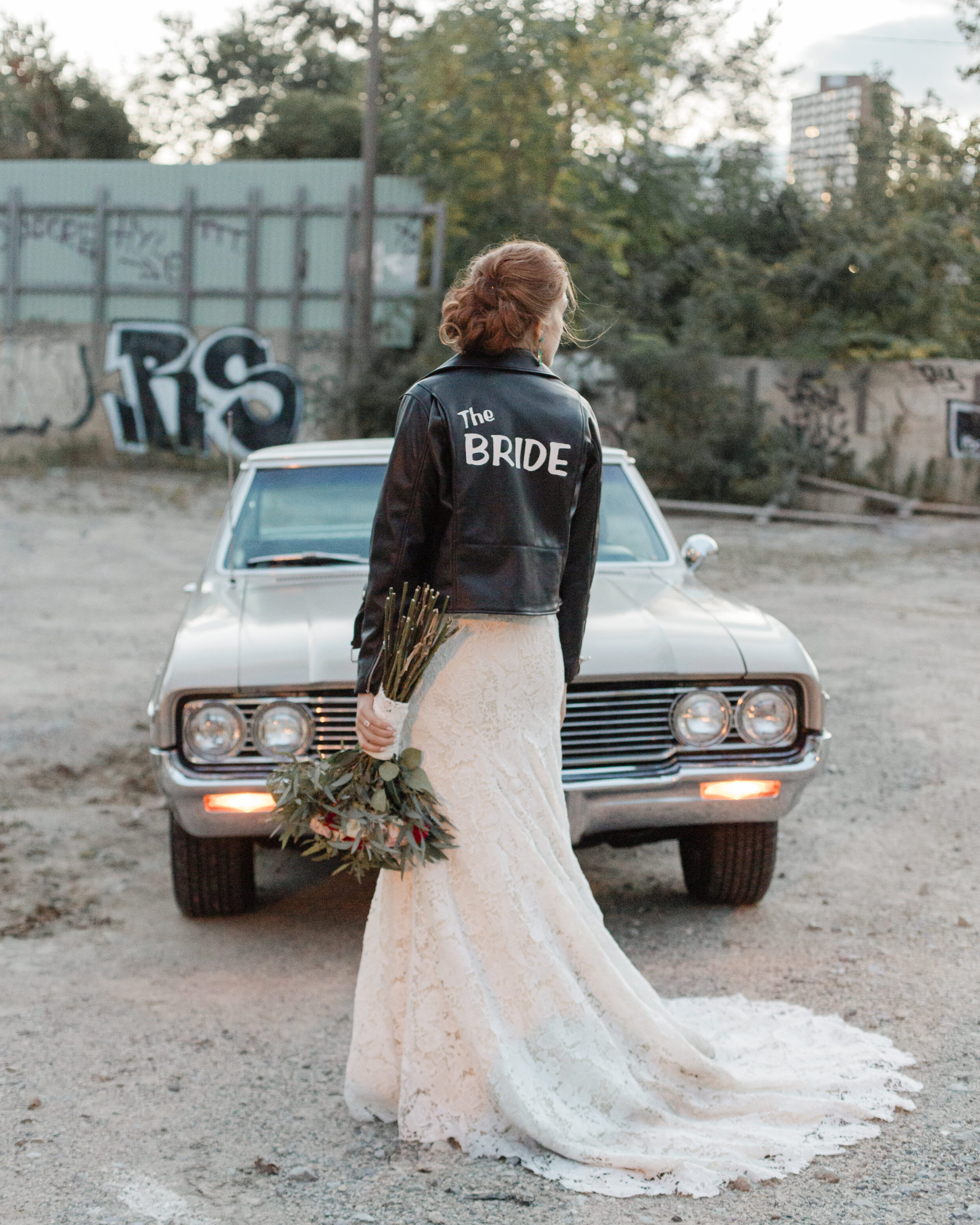 A woman holds a floral bouquet wearing a leather jacket that says bride. 