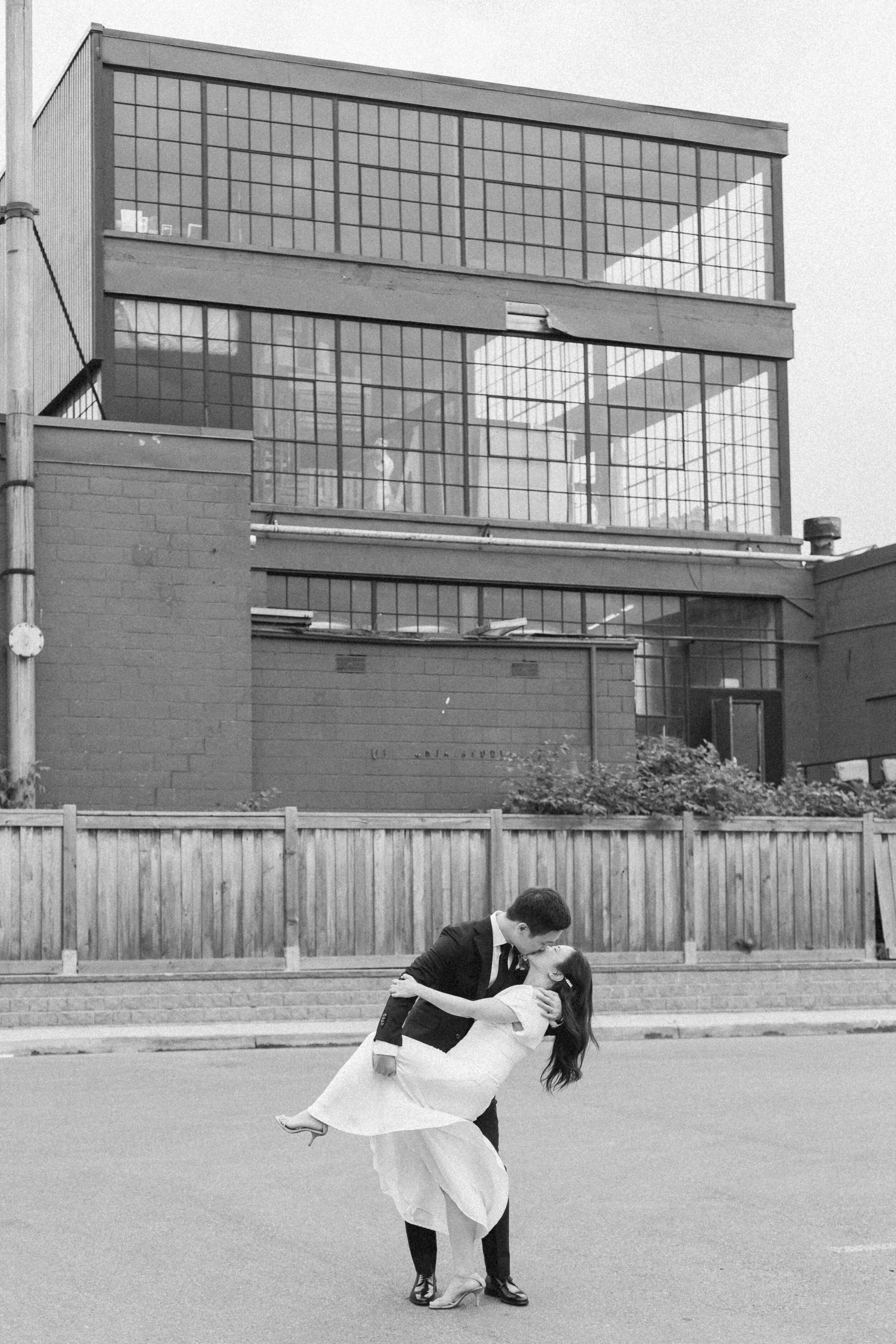 A newlywed couple poses in front of a glass window building in Toronto. 