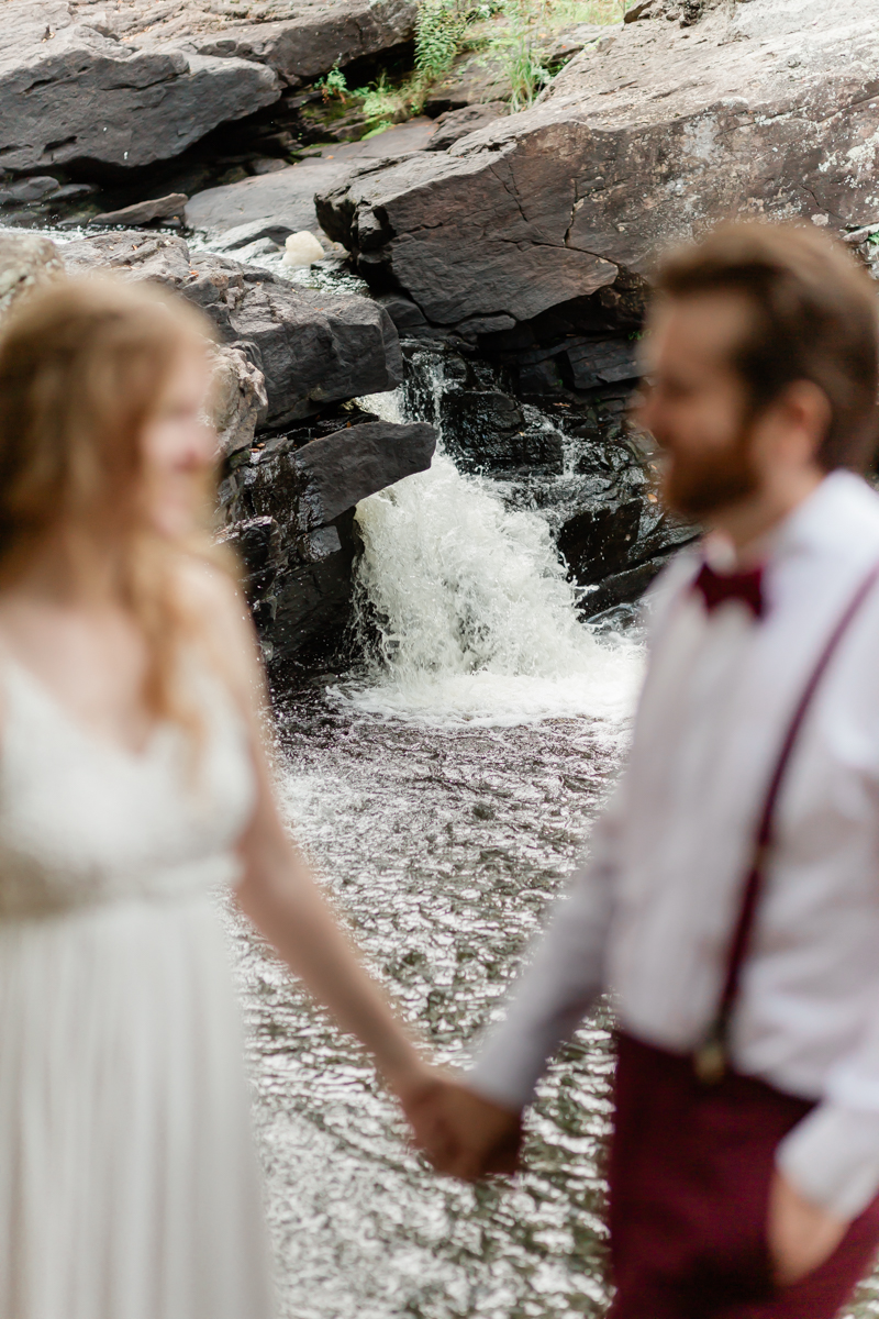 A couple holding hands in front of a waterfall during their Algonquin Park elopement 